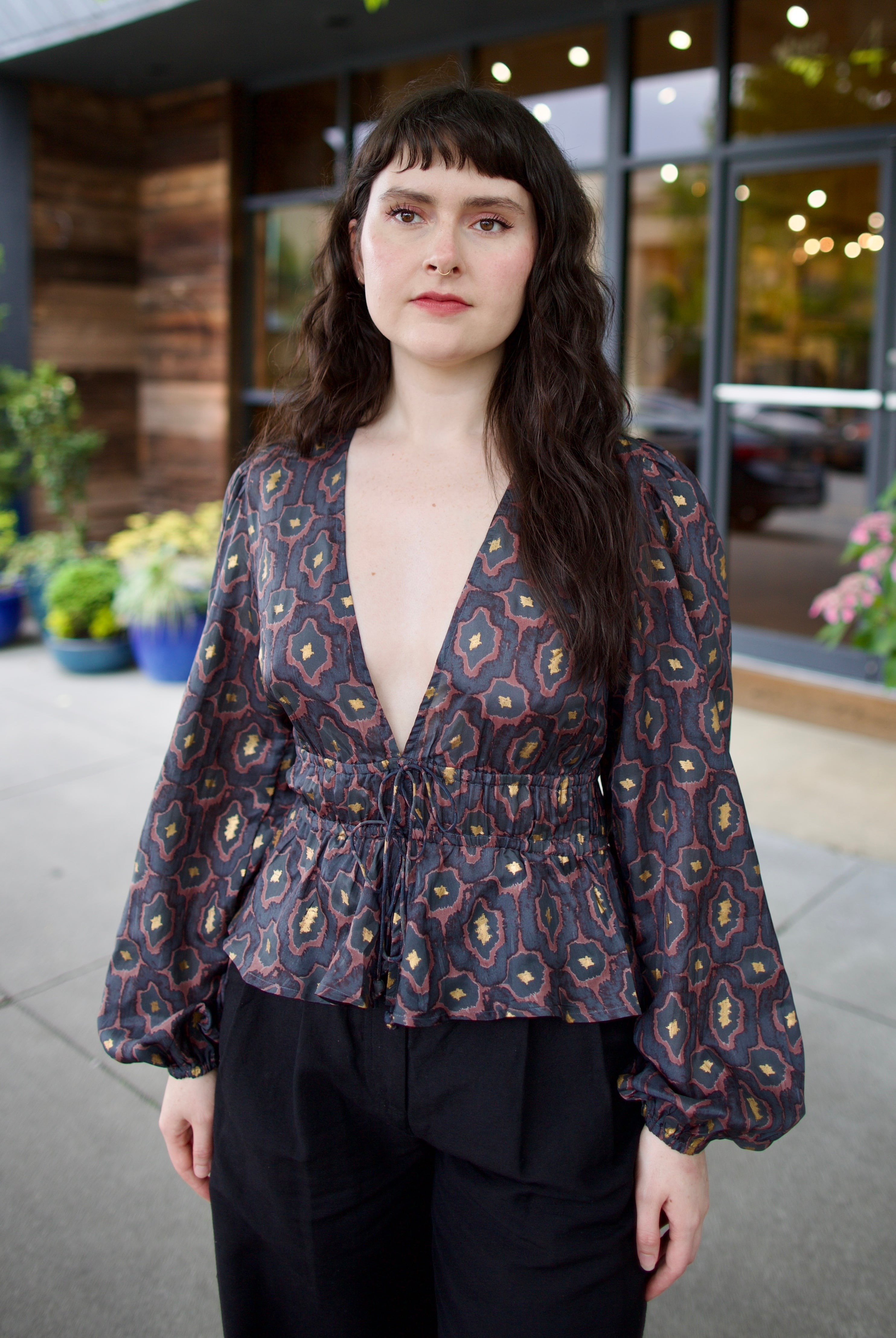 Image of a woman wearing the Hannah Artwear silk Lola Blouse with peplum, long sleeves, v-neck, blockprint and hand applied gold leaf