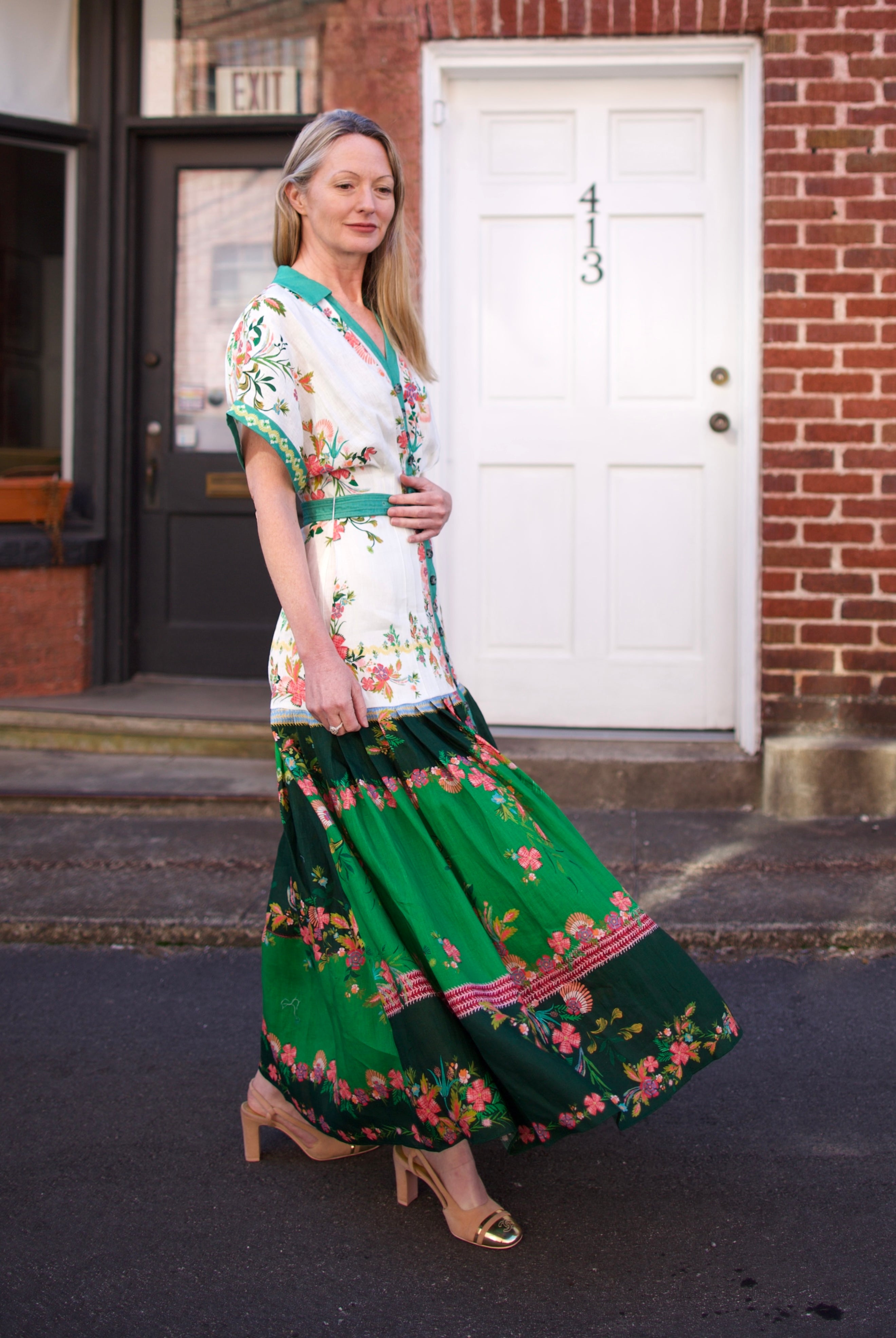 Mature woman wearing luxury women's Saloni Riya B linen dress with button front, rolled short sleeves, removable belt, and drop waist flowy skirt