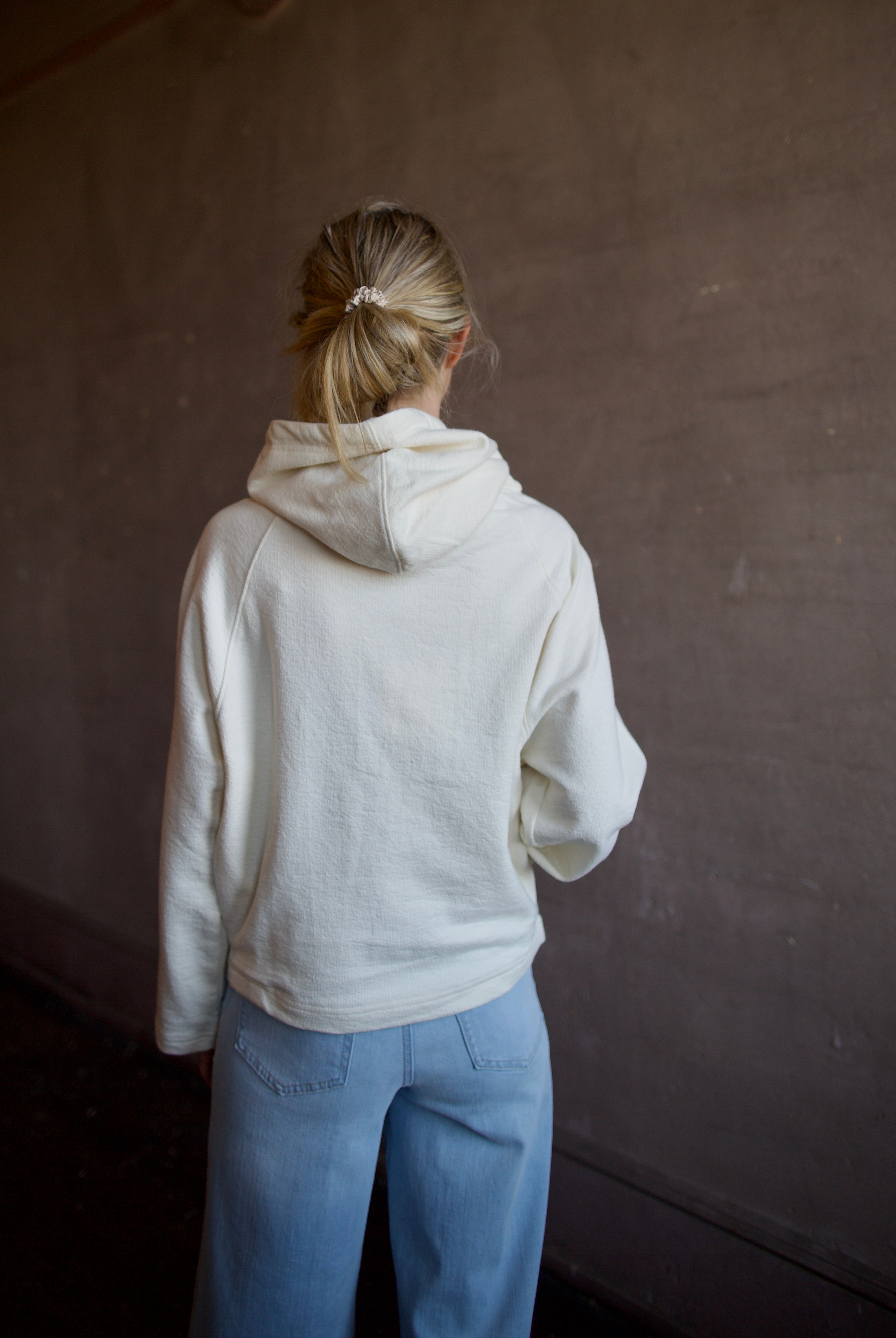 Mature woman wearing luxury TWP Ali's ivory Hoodie featuring raglan sleeves and kangaroo pocket with boxy fit, delivering elevated comfort