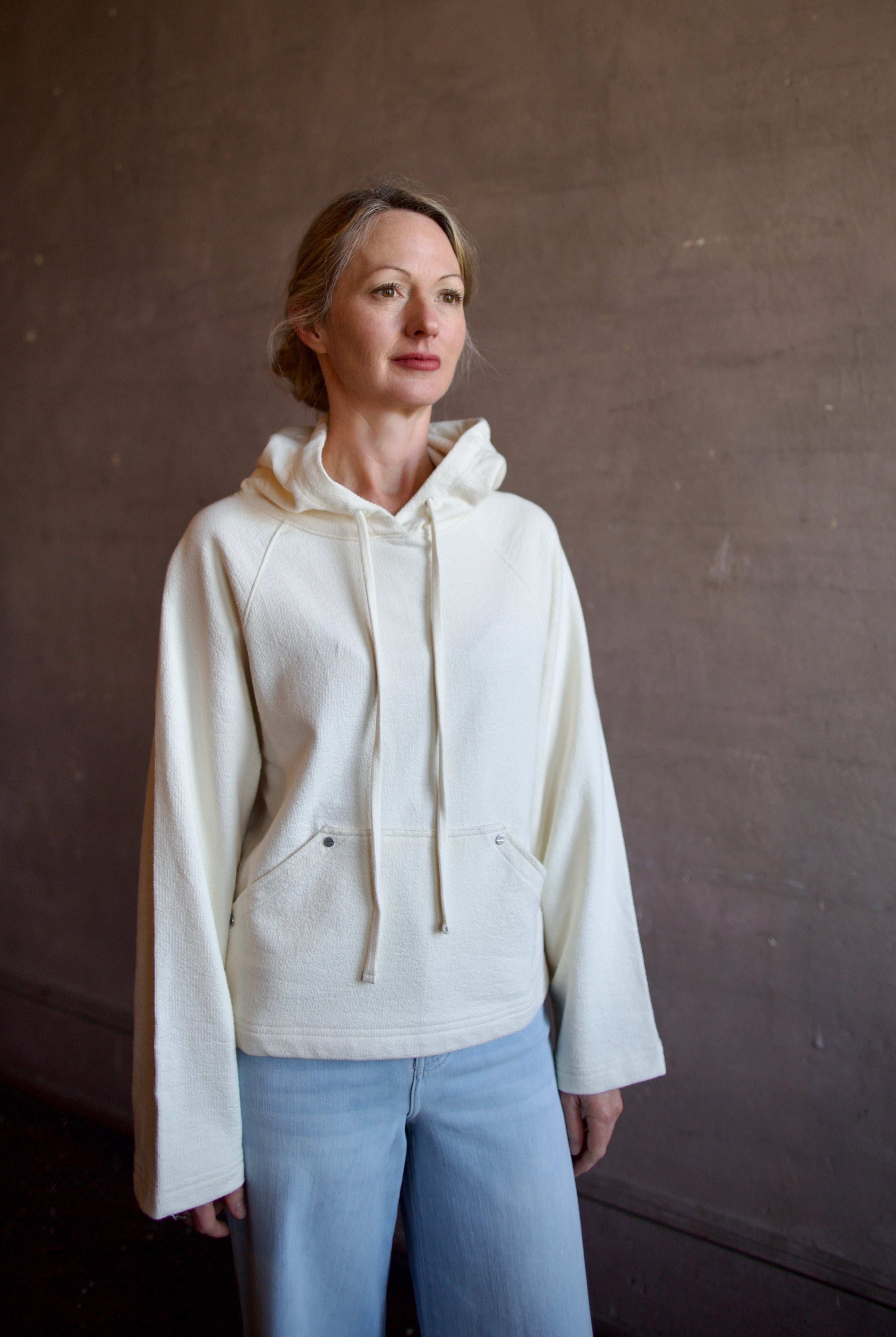 Mature woman wearing luxury TWP Ali's ivory Hoodie featuring raglan sleeves and kangaroo pocket with boxy fit, delivering elevated comfort