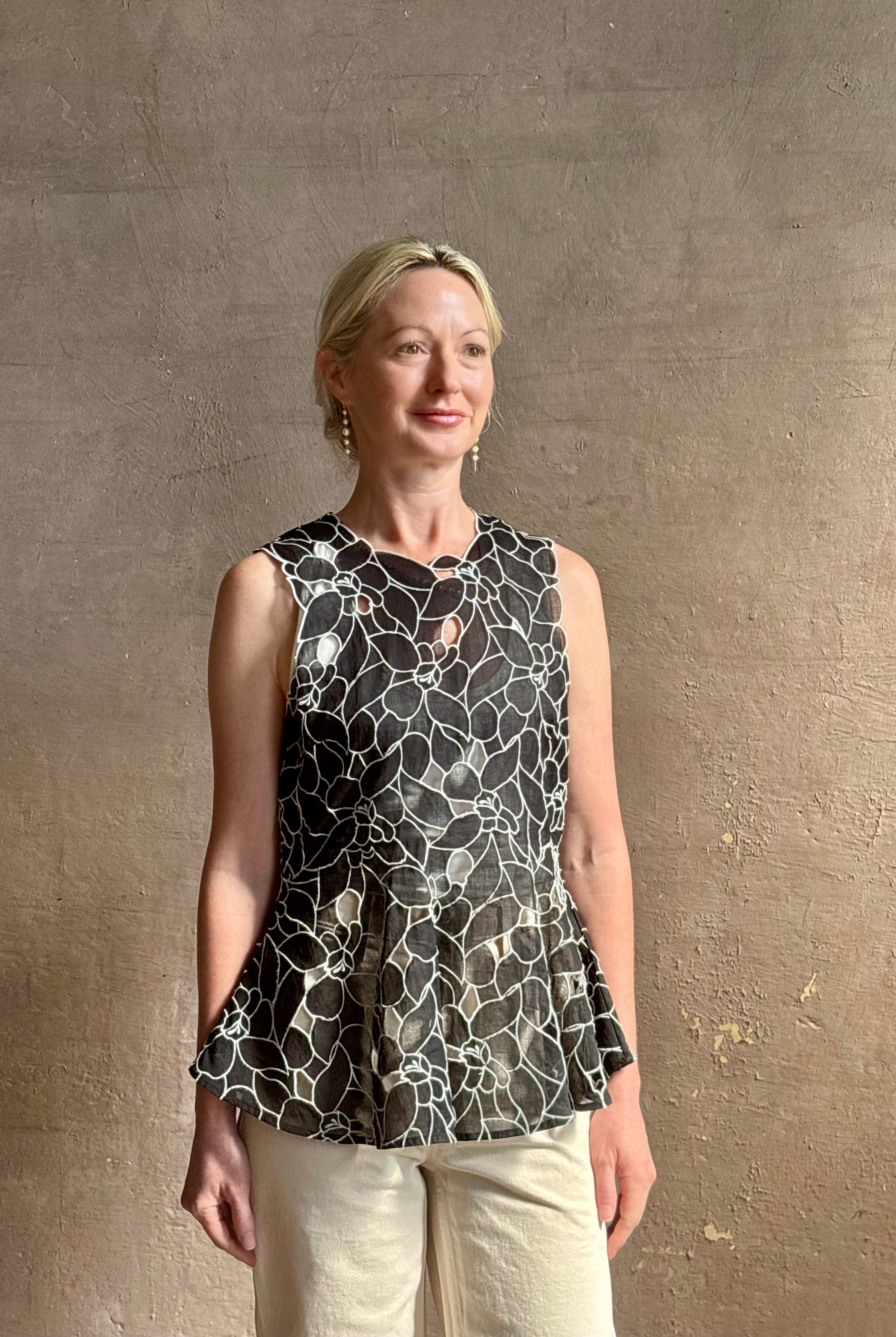 Mature woman wearing the Ulla Johnson Ali Sleeveless black cotton peplum top with contrast white embroidery for ultimate feminine sophistication