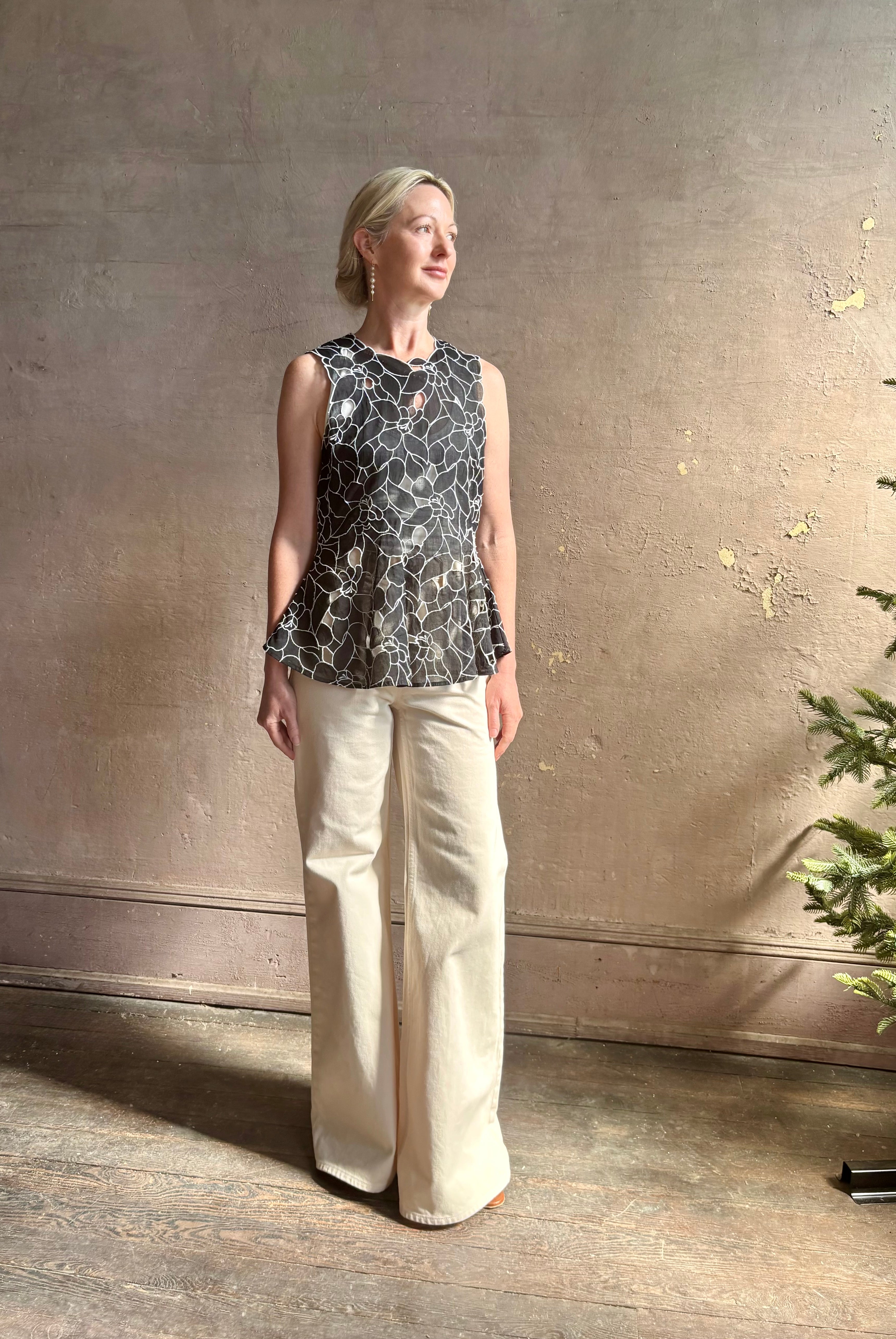 Mature woman wearing the Ulla Johnson Ali Sleeveless black cotton peplum top with contrast white embroidery for ultimate feminine sophistication