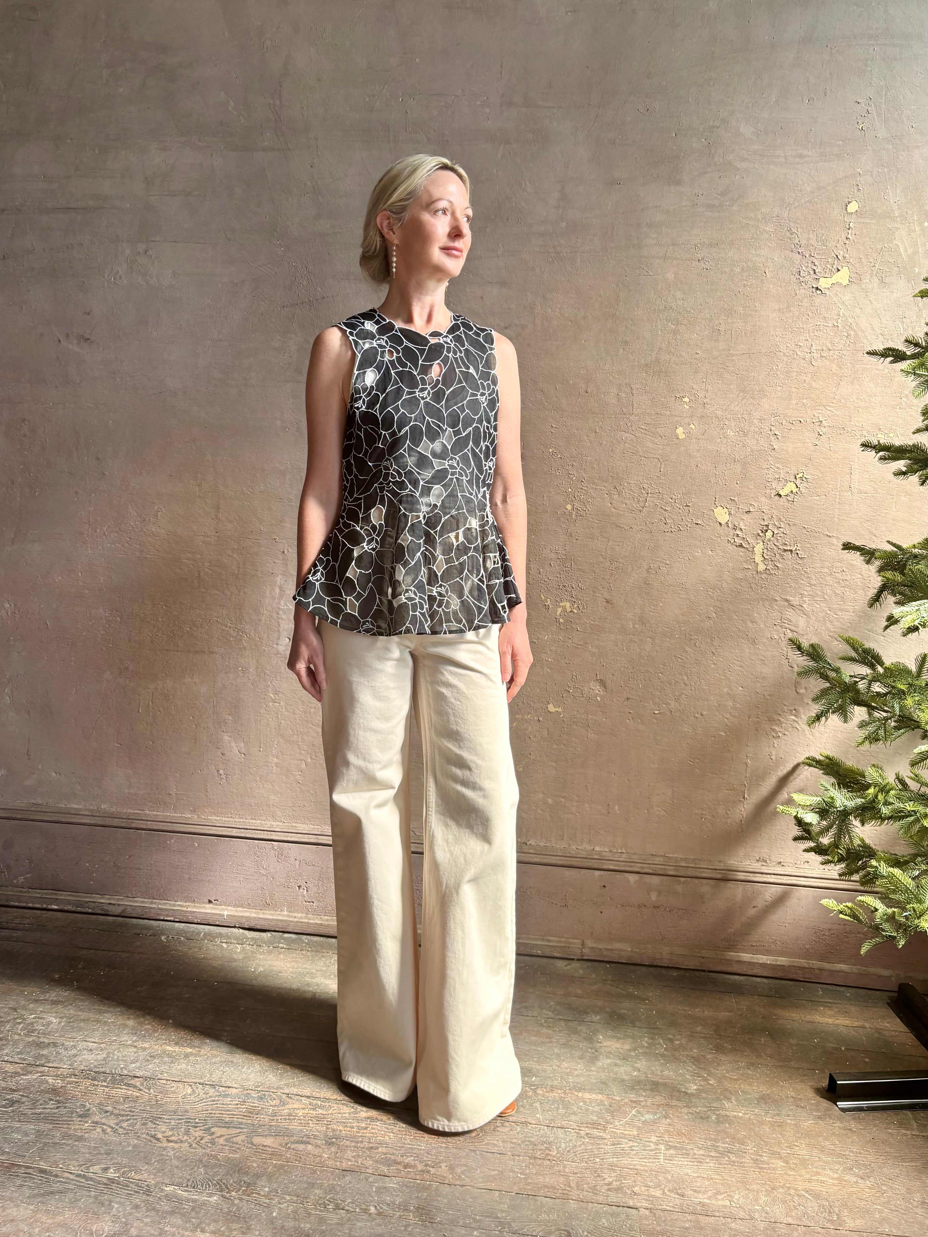 Mature woman wearing the Ulla Johnson Ali Sleeveless black cotton peplum top with contrast white embroidery for ultimate feminine sophistication