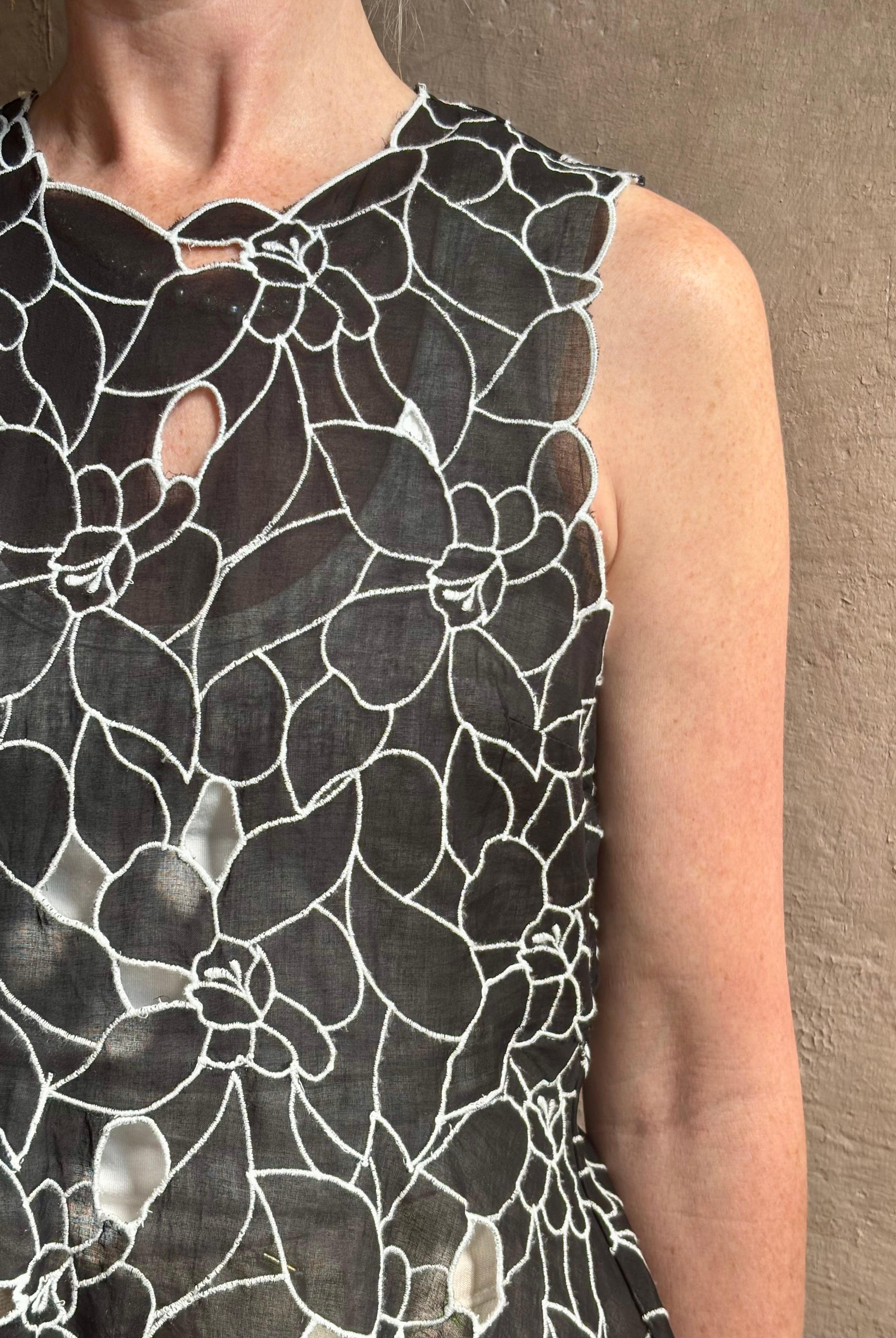 Mature woman wearing the Ulla Johnson Ali Sleeveless black cotton peplum top with contrast white embroidery for ultimate feminine sophistication