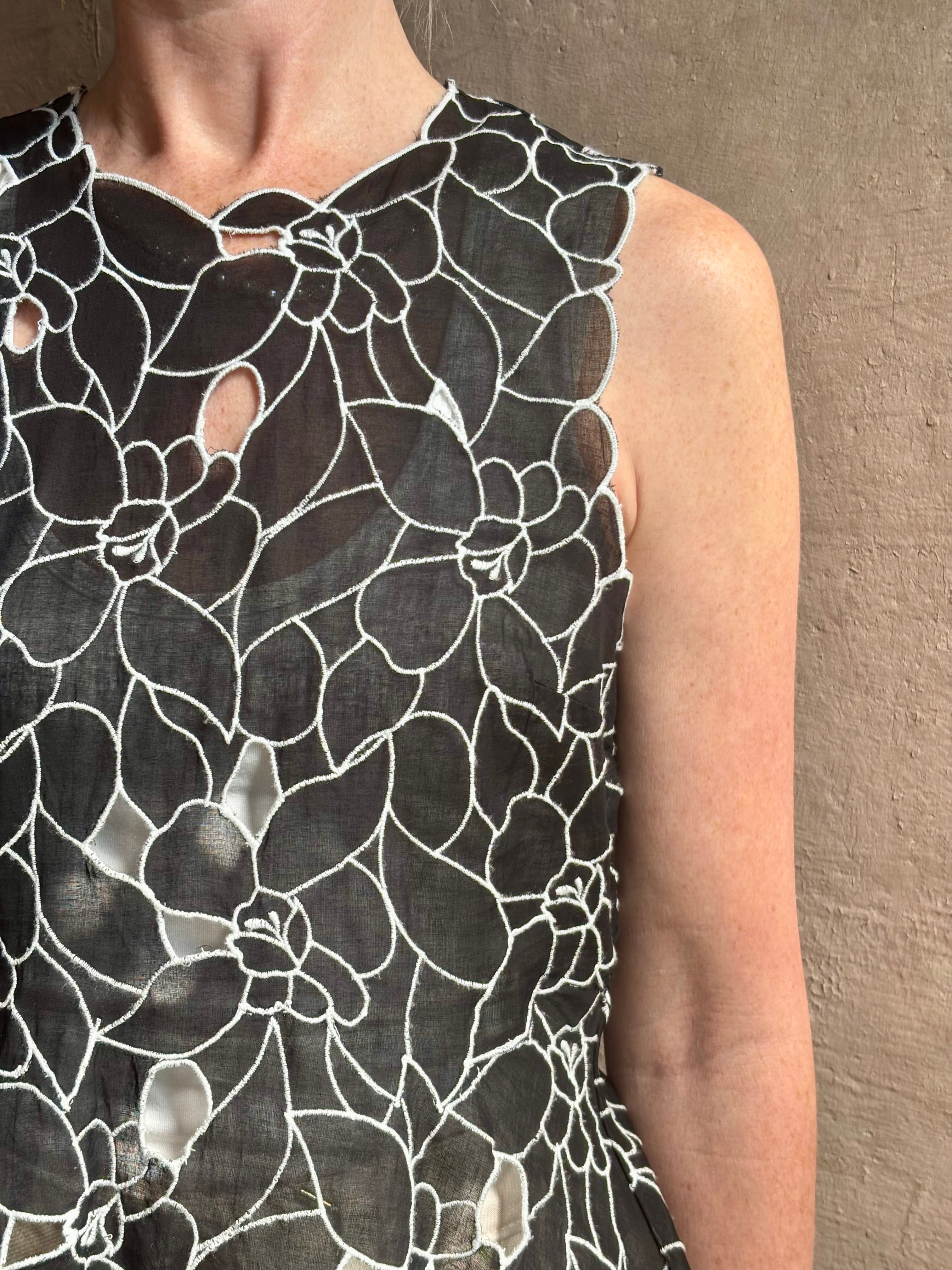 Mature woman wearing the Ulla Johnson Ali Sleeveless black cotton peplum top with contrast white embroidery for ultimate feminine sophistication