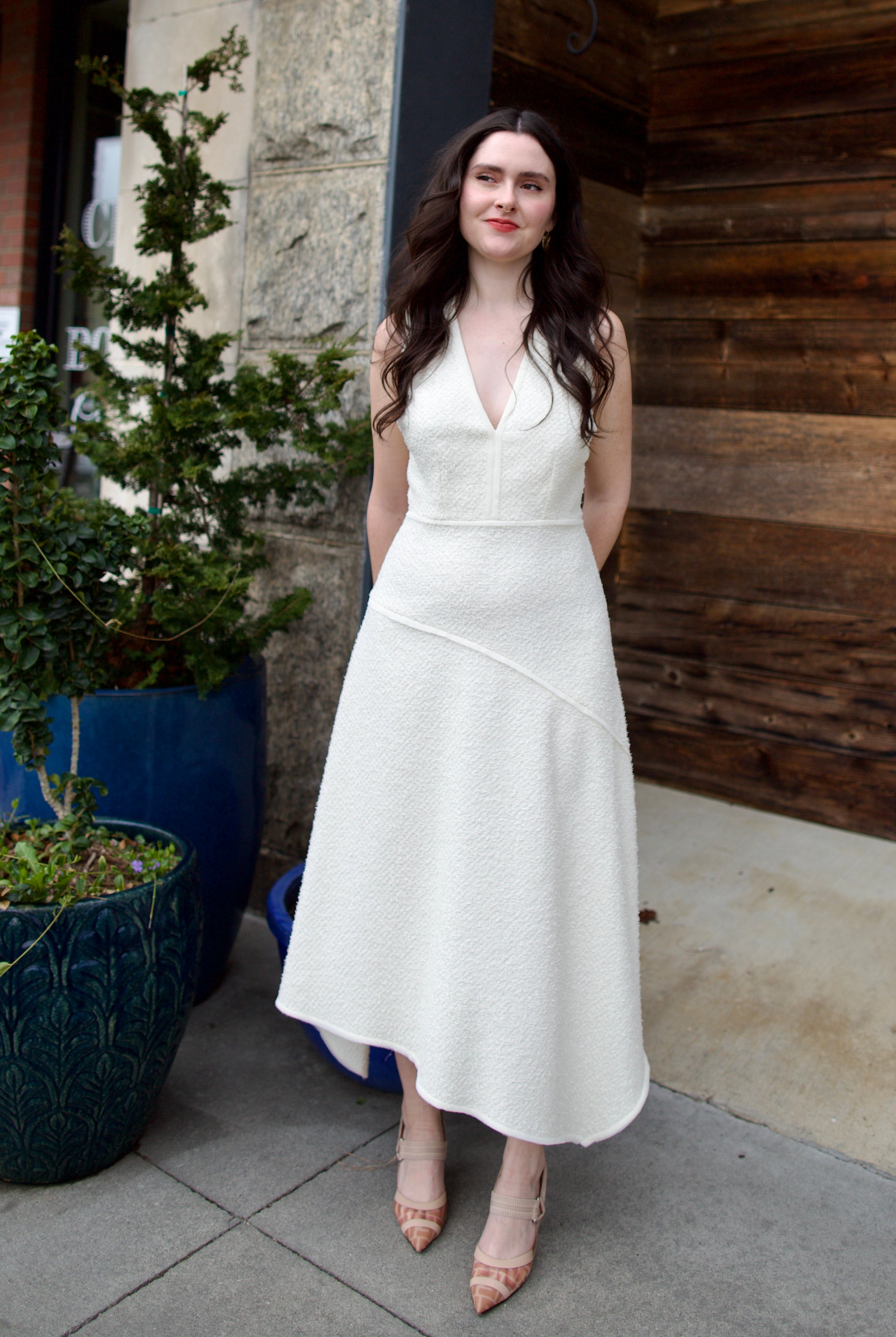 Woman wearing the Ulla Johnson Florence Dress in textured off-white cotton blend with a v-neckline and asymmetrical hem