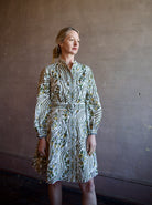 Mature woman wearing luxury women's linen Nolan dress by Veronica Beard featuring button front removable belt long sleeves and knee length skirt