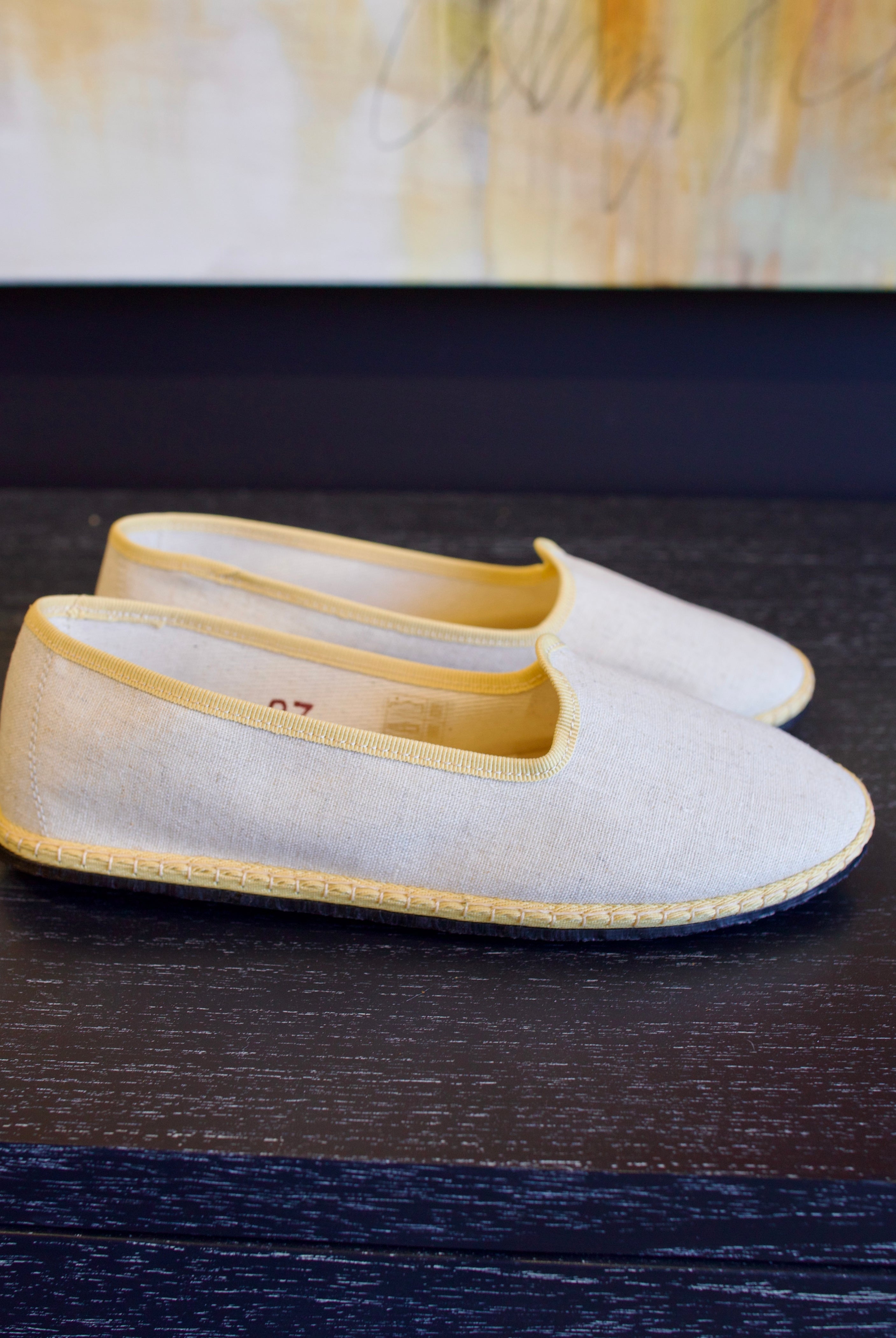 A pair of beige Vibi Venezia slippers with yellow grosgrain ribbon trim in premium linen construction and traditional Venetian slipper design
