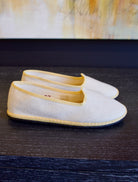 A pair of beige Vibi Venezia slippers with yellow grosgrain ribbon trim in premium linen construction and traditional Venetian slipper design