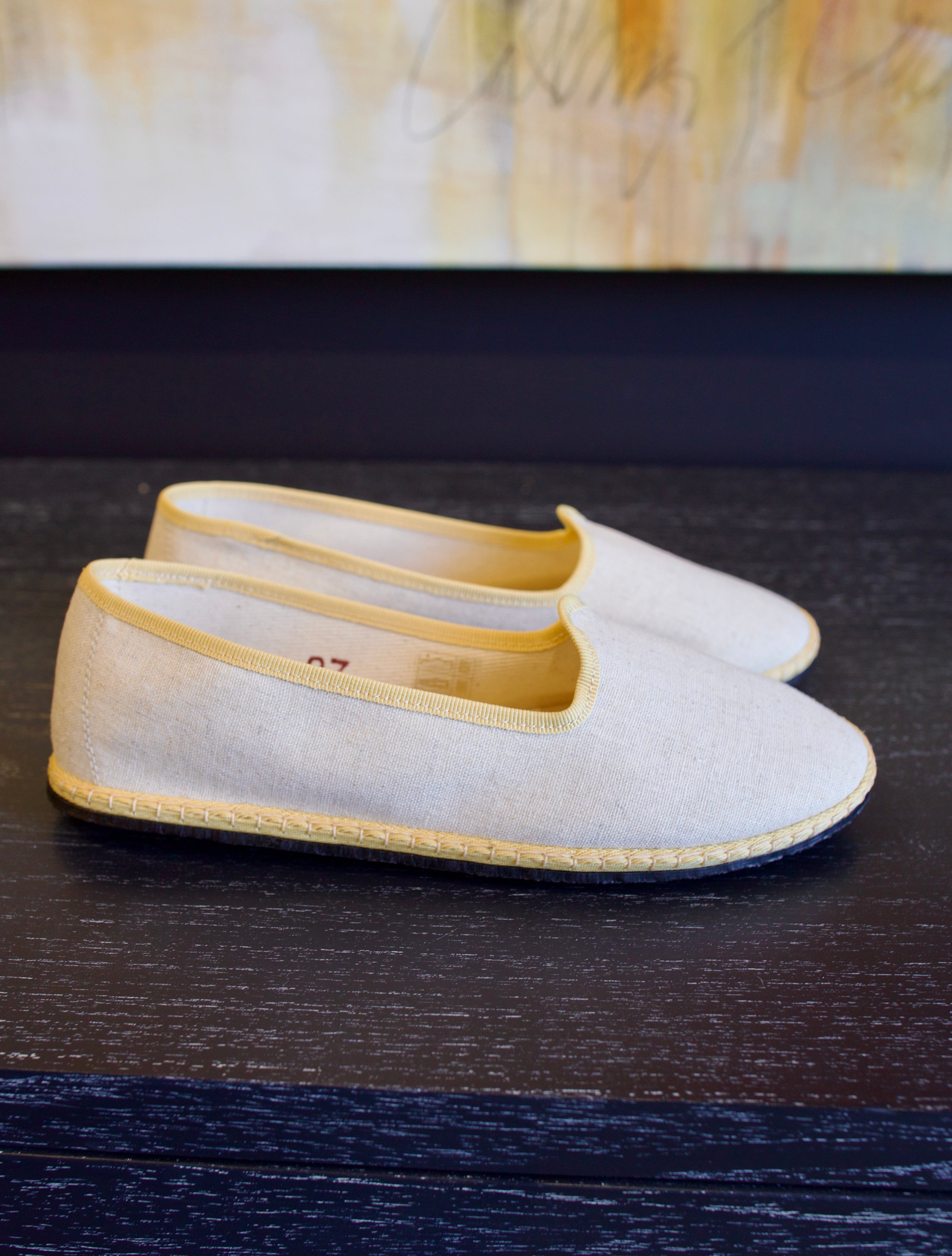A pair of beige Vibi Venezia slippers with yellow grosgrain ribbon trim in premium linen construction and traditional Venetian slipper design