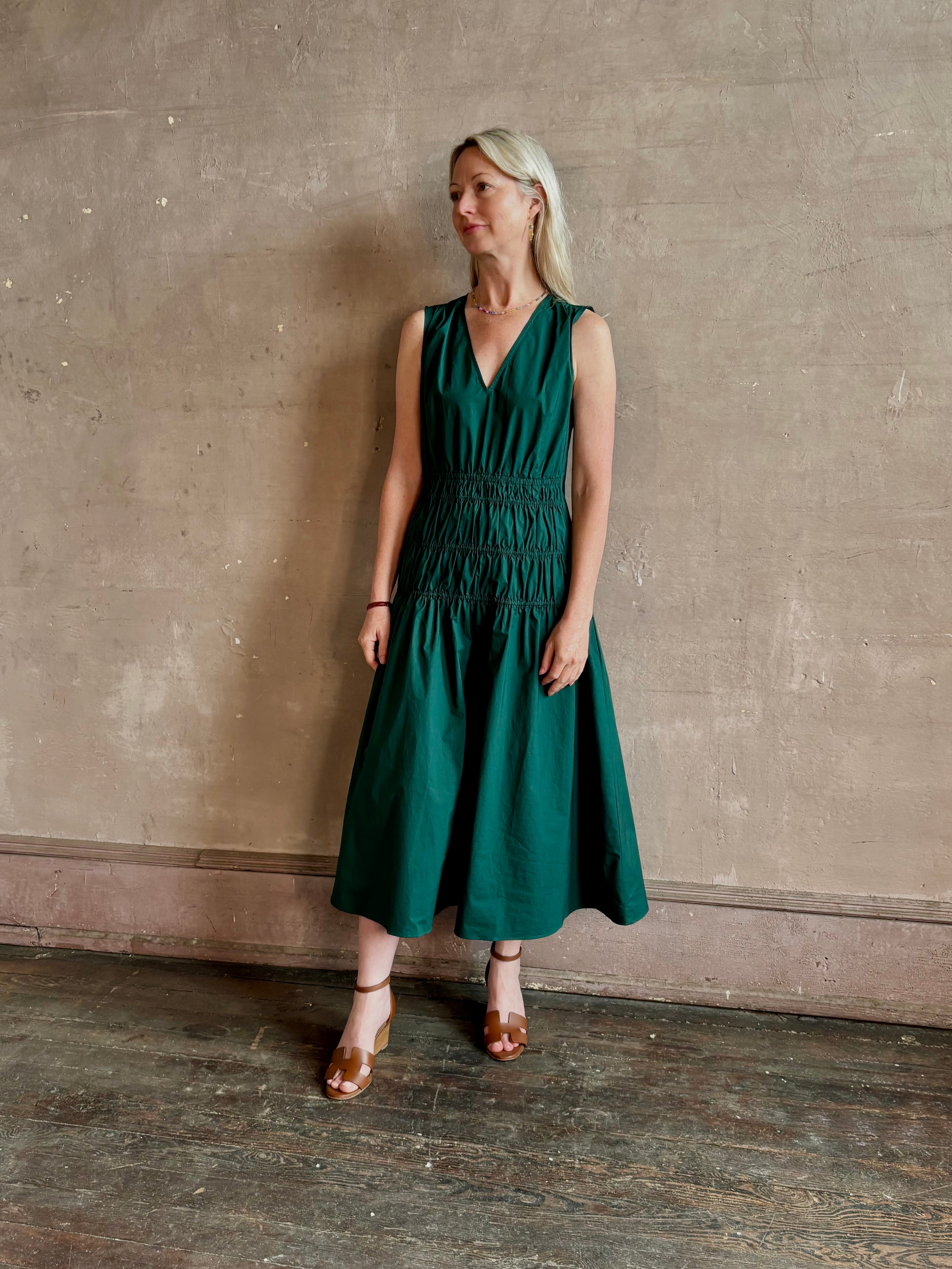 Mature woman wearing Loren Dress from Proenza Schouler White Lable rendered in aspruce green and crafted from a cotton elastane blend with v-neck, sleeveless, pockets, and rushed waist
