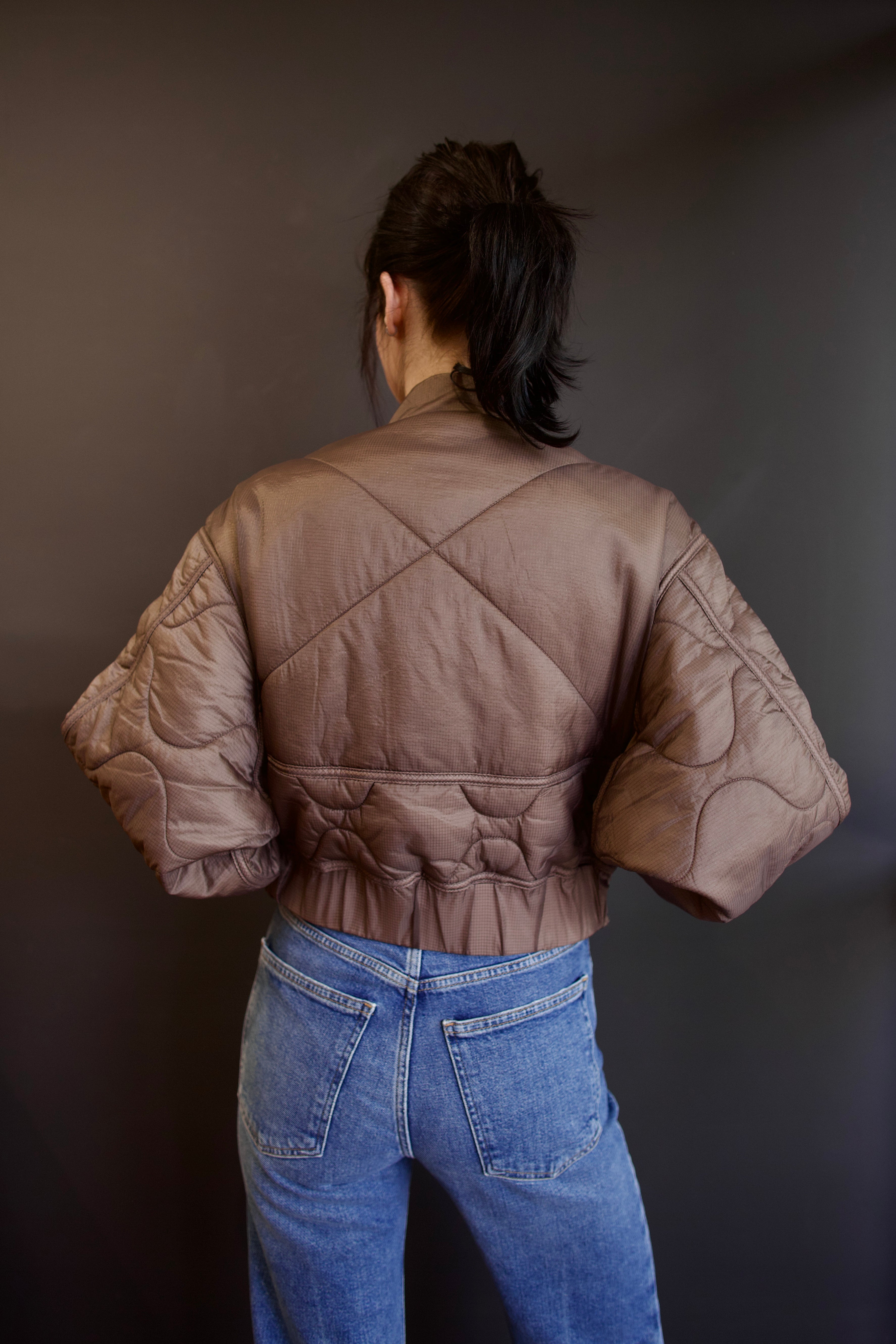Model wearing Agolde Iona quilted jacket in brown with circular and x stitch details on back with gathered waist