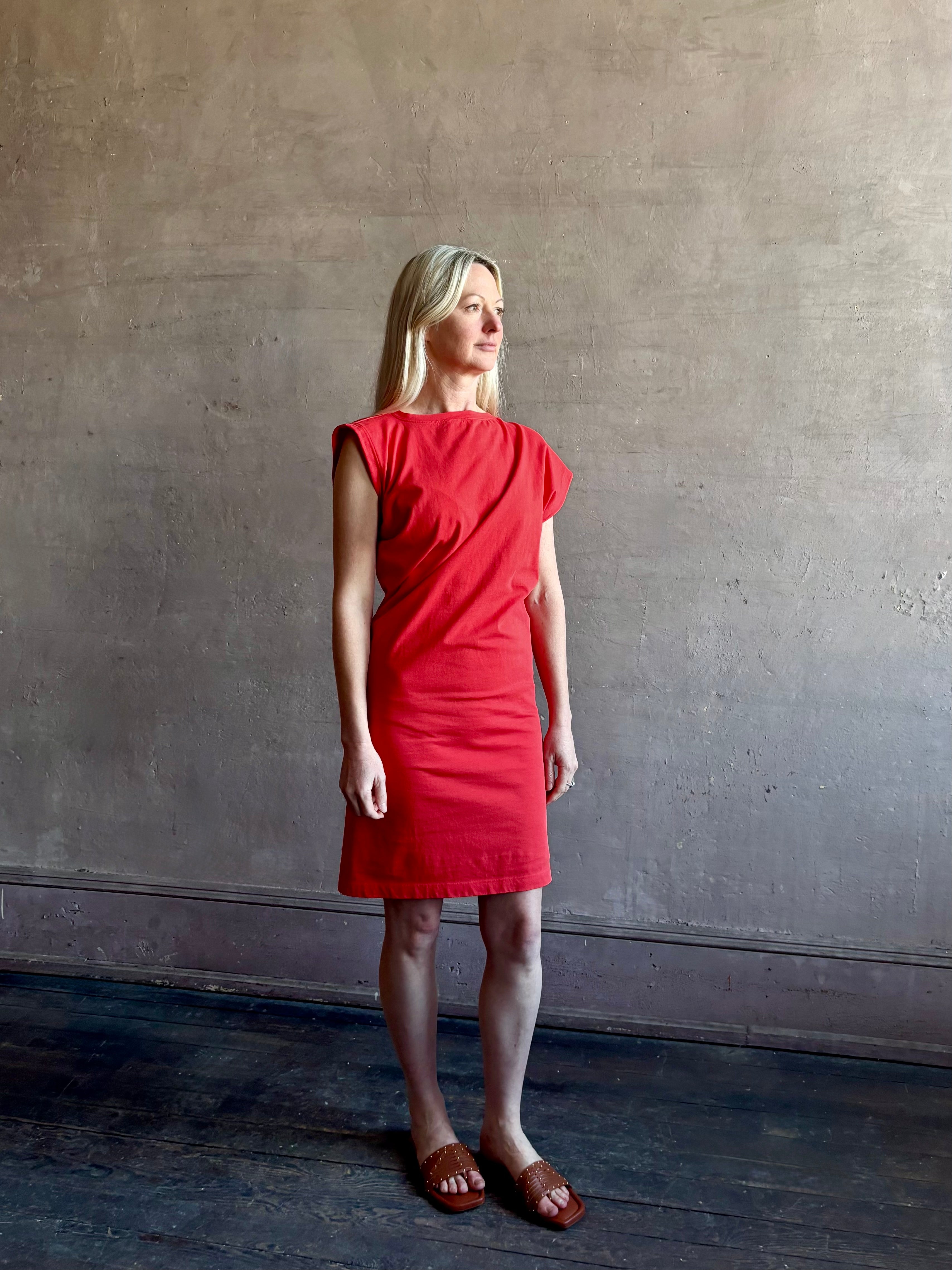 Woman wearing the red Beth Dress from Agolde crafted from 100% cotton with short sleeves, knee length and asymmetrical twist draping in a effortless relaxed fit