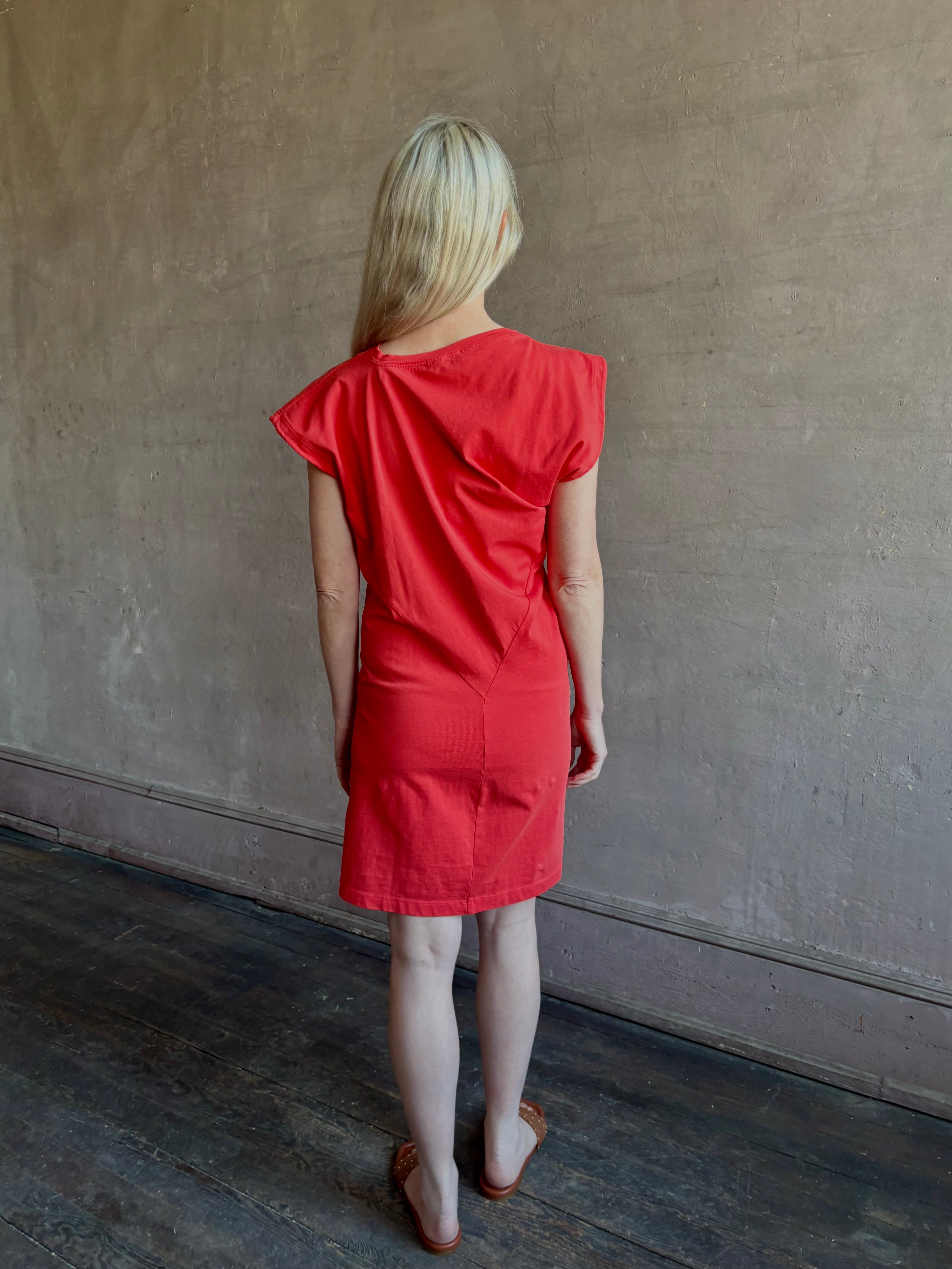 Woman wearing the red Beth Dress from Agolde crafted from 100% cotton with short sleeves, knee length and asymmetrical twist draping in a effortless relaxed fit