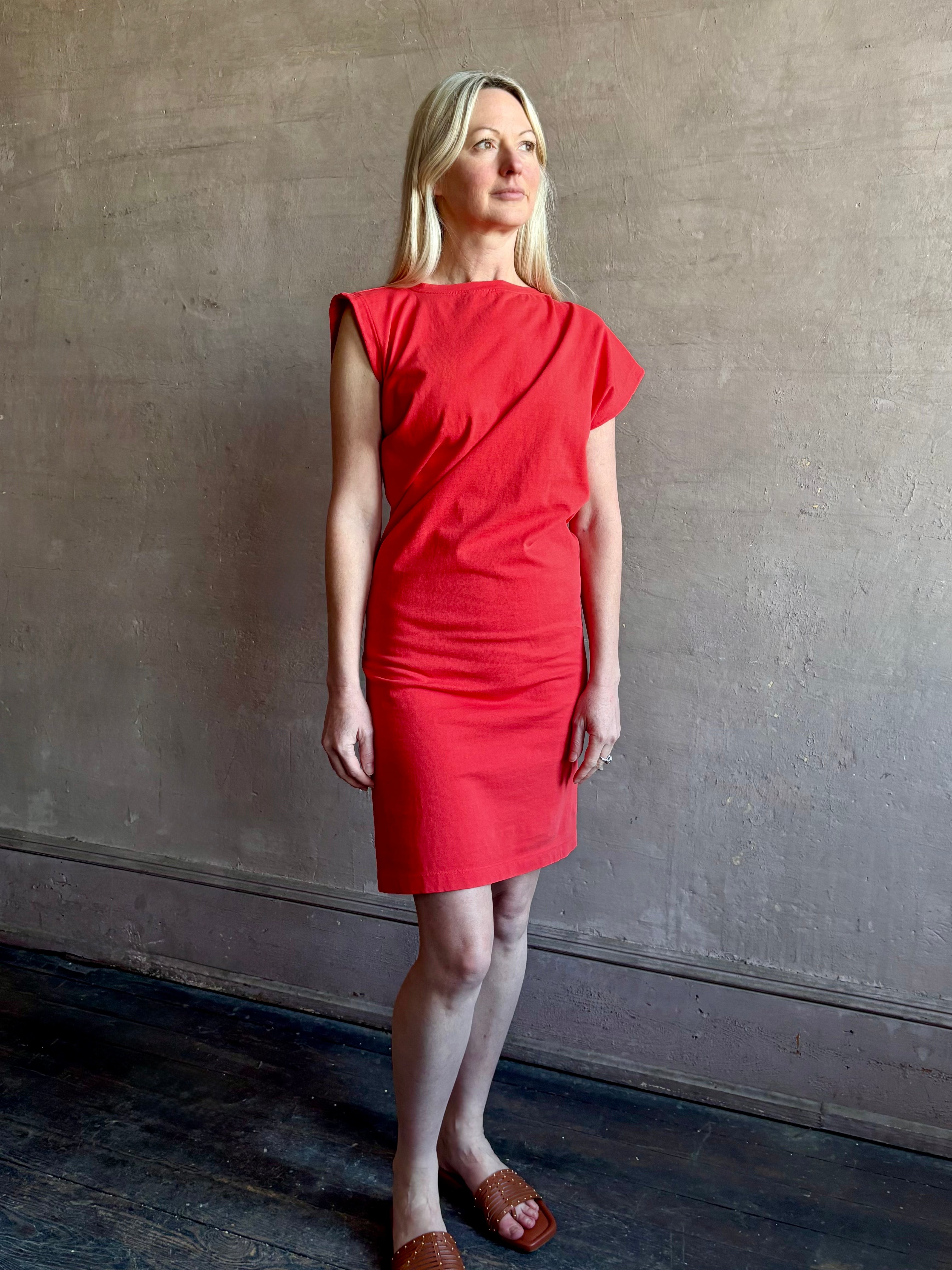 Woman wearing the red Beth Dress from Agolde crafted from 100% cotton with short sleeves, knee length and asymmetrical twist draping in a effortless relaxed fit