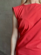 Woman wearing the red Beth Dress from Agolde crafted from 100% cotton with short sleeves, knee length and asymmetrical twist draping in a effortless relaxed fit