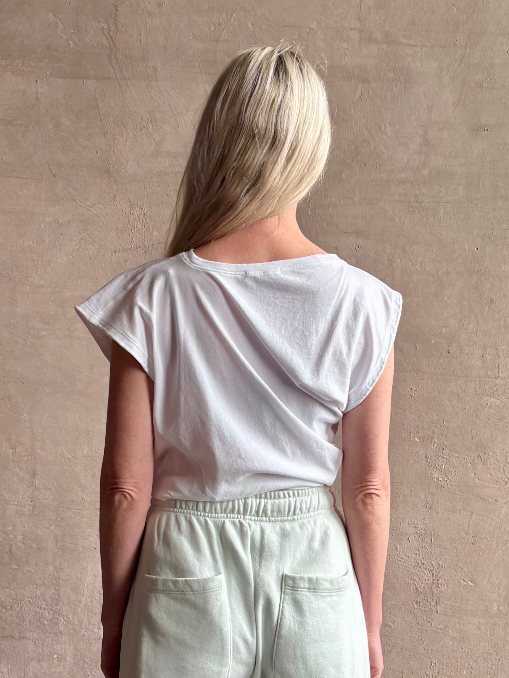 Mature woman wearing a white asymmetrical beth tee shirt from Agolde  with short sleeves, crew neckline and architectural draping