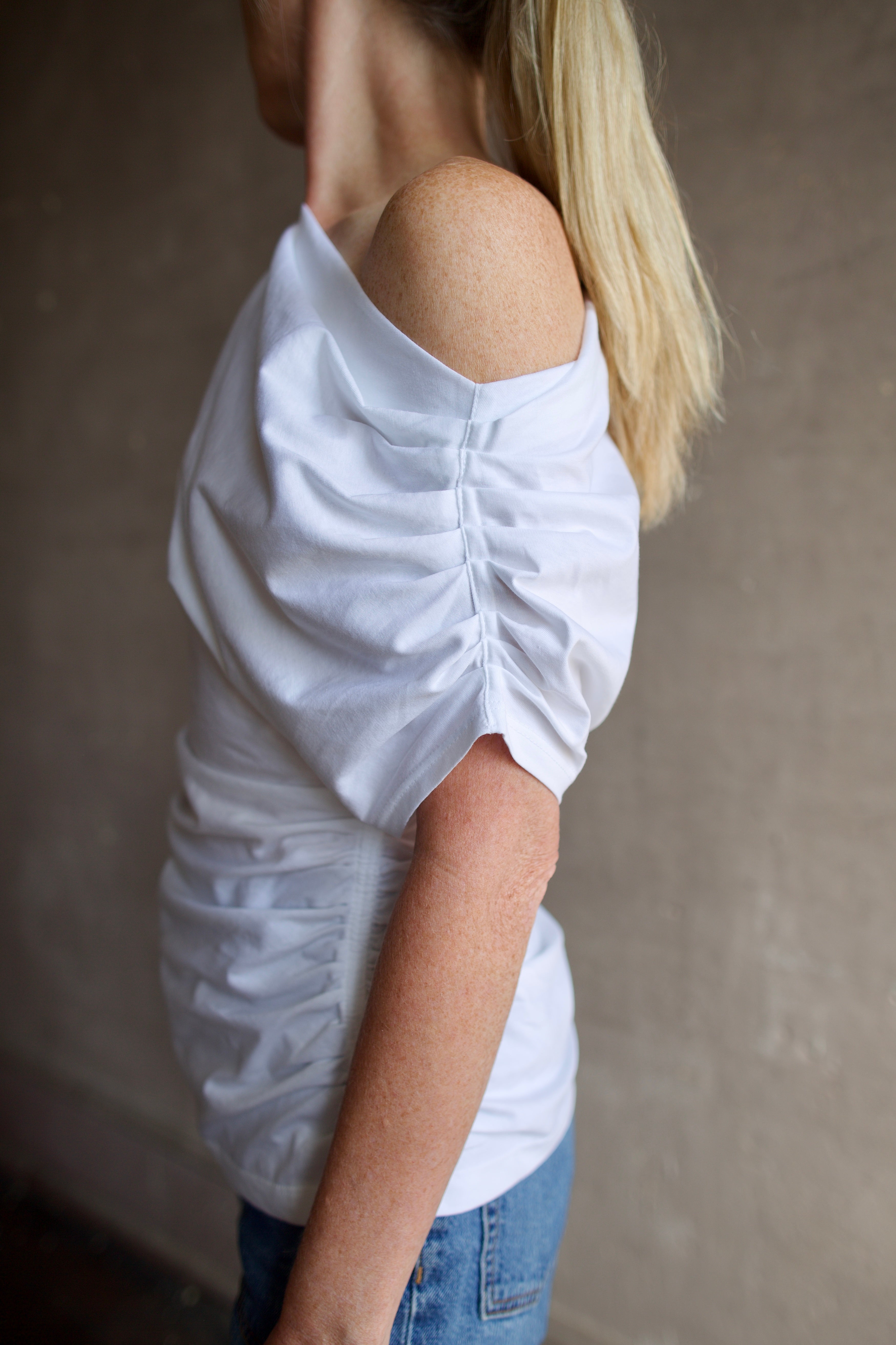 Model wearing white ALC Alice cotton t-shirt with rushed sides and shoulder detail that can be worn asymmetrically