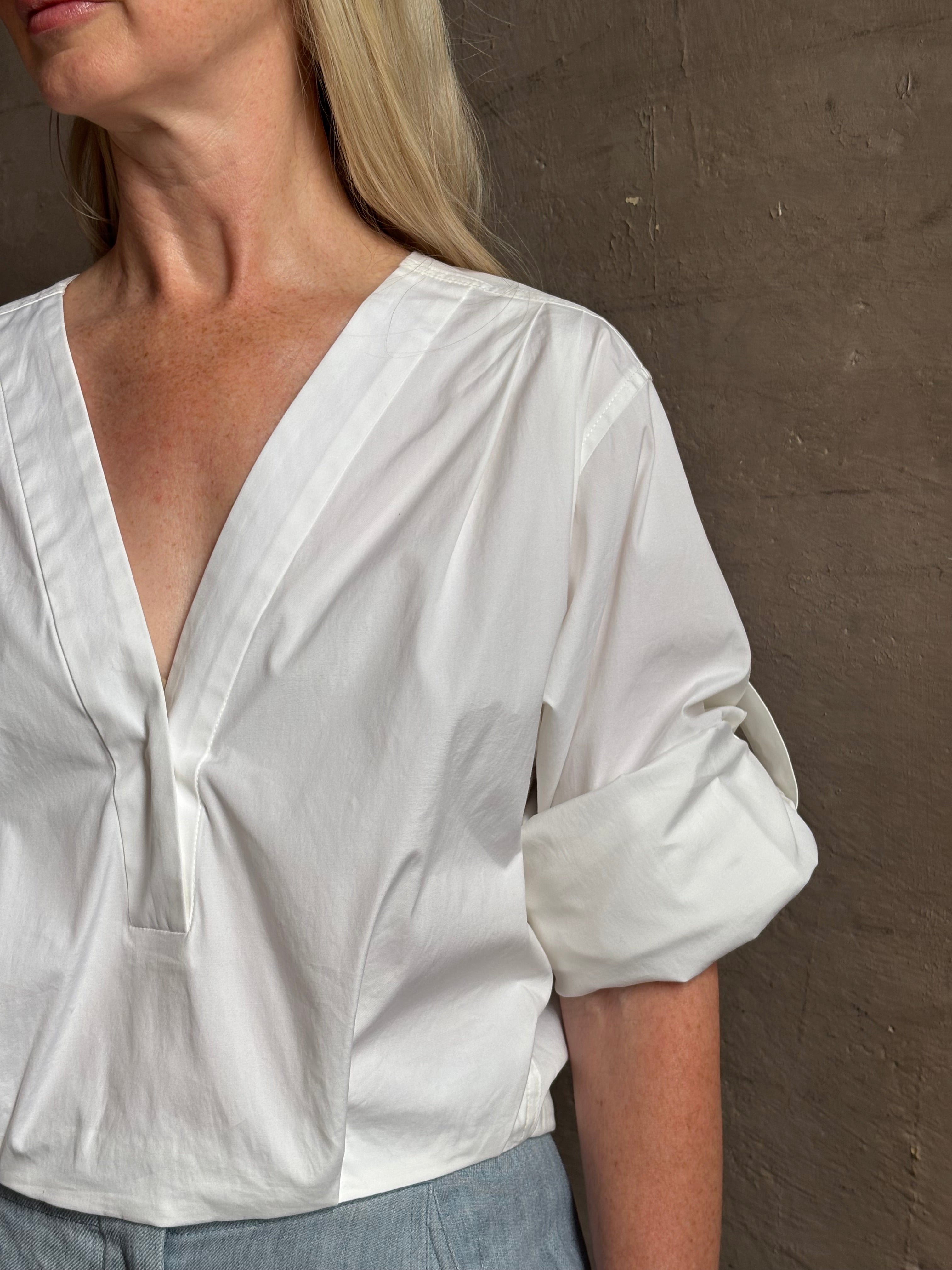 Mature woman wearing The A.L.C. Jordan Top in White Long sleeve blouse boasts premium cotton blend with v-neck and tab to roll sleeves up to a half sleeve