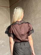 Image of mature woman wearing ALC Luna top in premium chocolate brown viscose blouse with a boat neck short sleeve and refined black lace trim