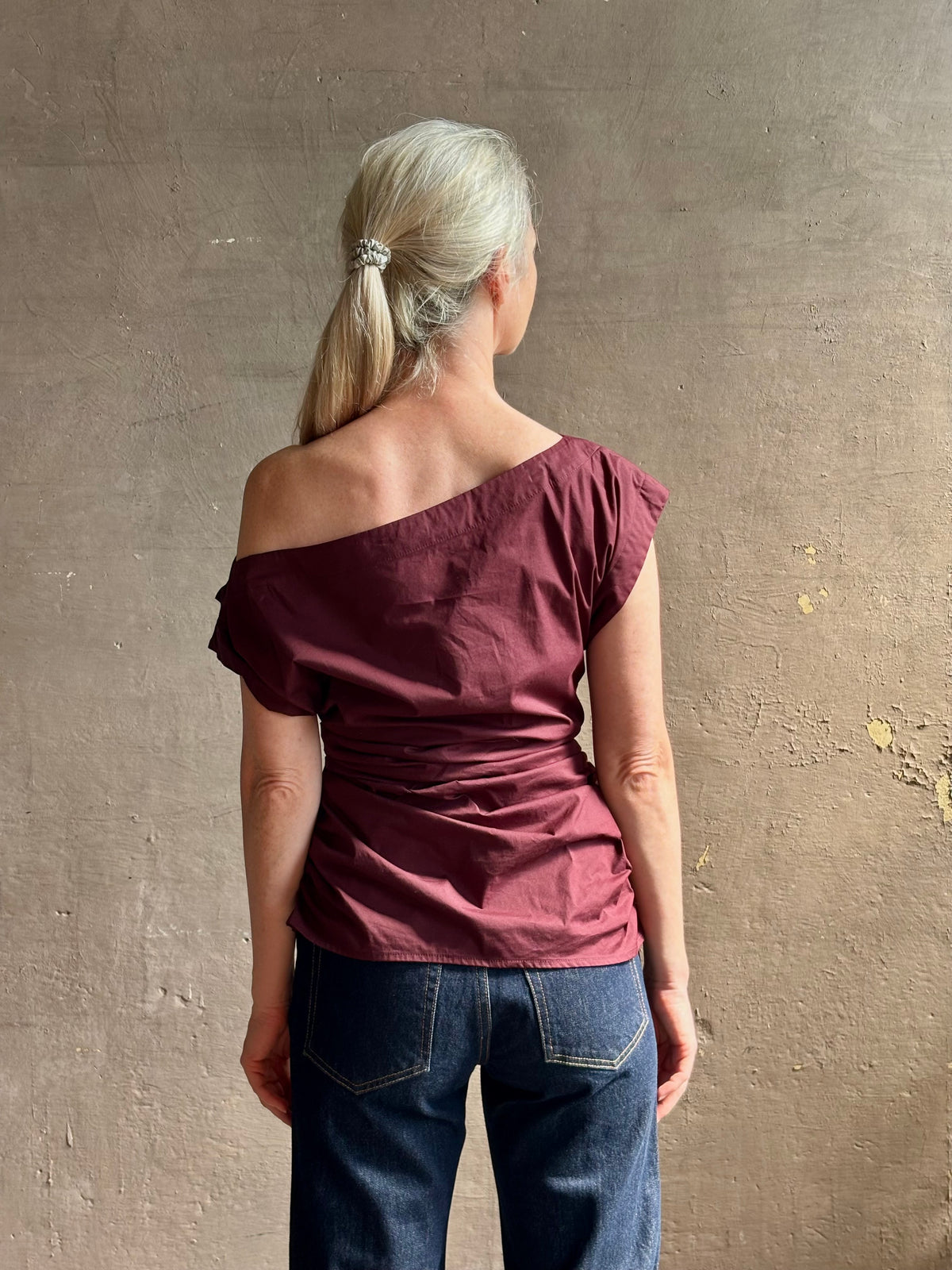 Mature woman wearing A.L.C.'s Nara Top in burgundy cotton poplin cold shoulder draping feminine cosmopolitan tailoring