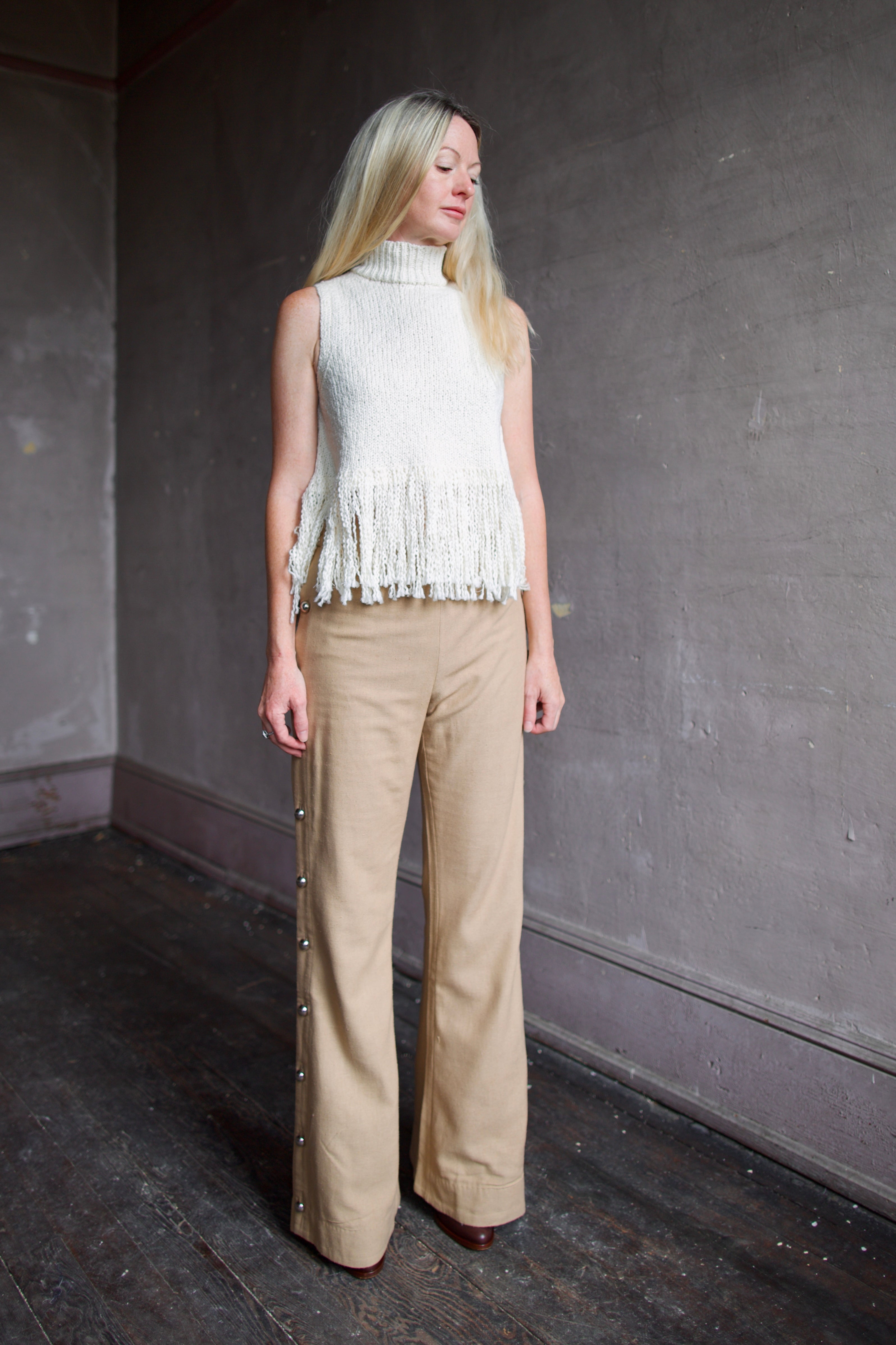 Model wearing an Alix of Bohemia cream sleeveless cotton sweater with fringe trimmed and silk trousers