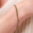 Image of a woman wearing a vivid natural blue diamond row bracelet designed by NC fine jeweler Amali in warm 18K yellow gold