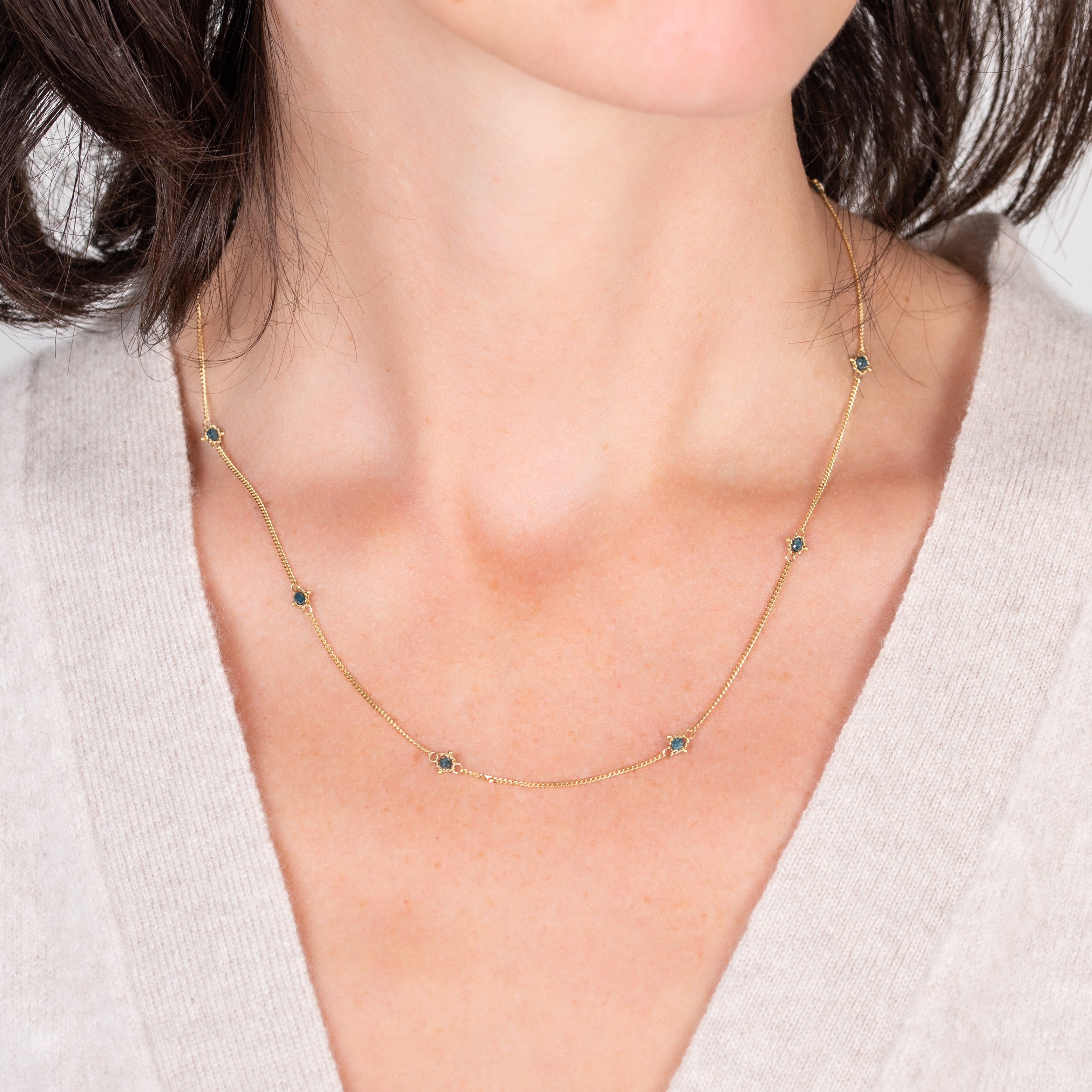 Image of a woman wearing a natural blue diamond chain necklace handcrafted by  North Carolina fine jewelry designer Amali in warm 18K yellow gold with a refreshing contemporary design