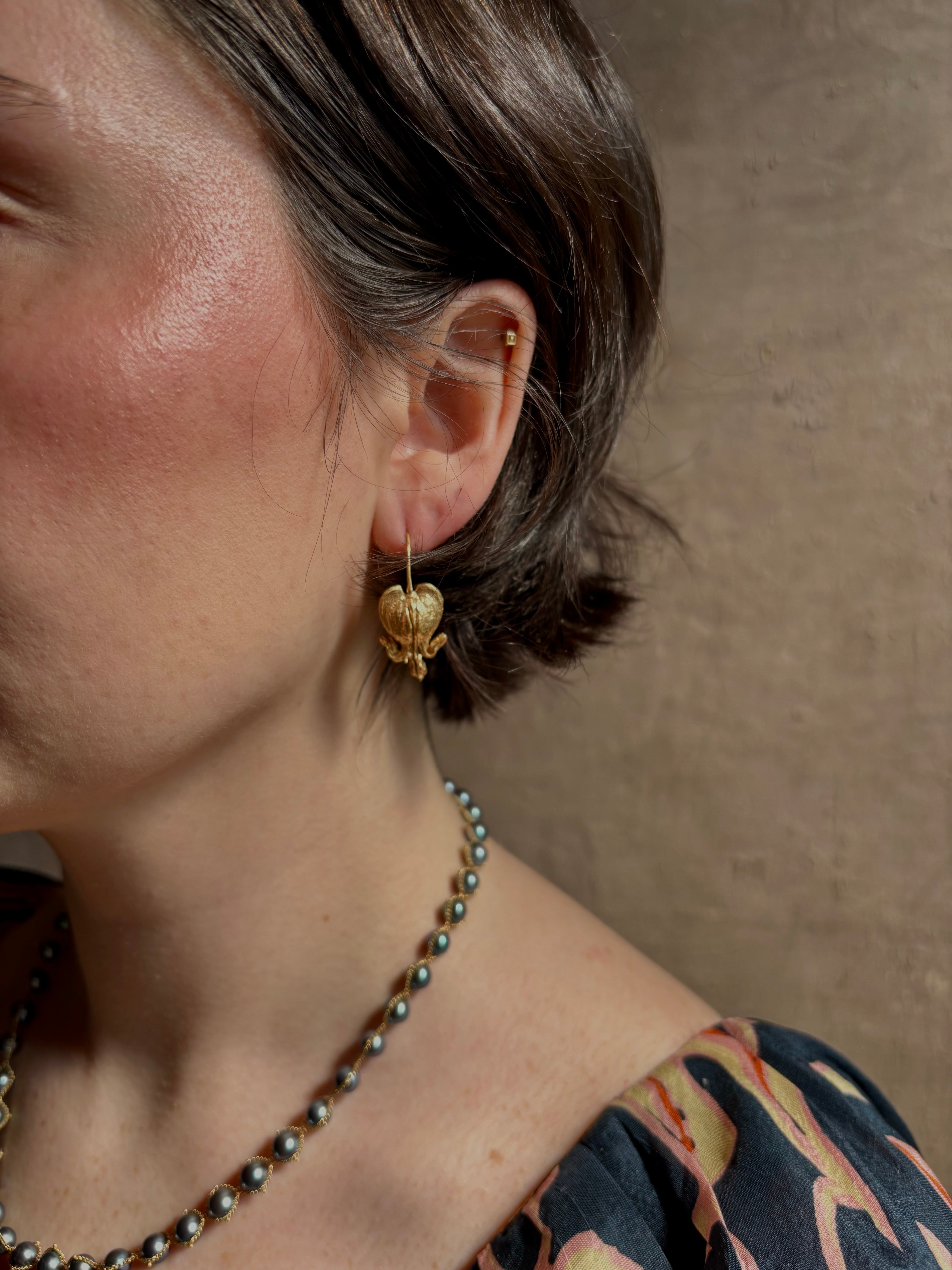 Woman wearing Bleeding Heart Hoop Earrings from North Carolina fine Jewelry artist Amber Mahler handcrafted 18K yellow gold vermeil botanical casting. 