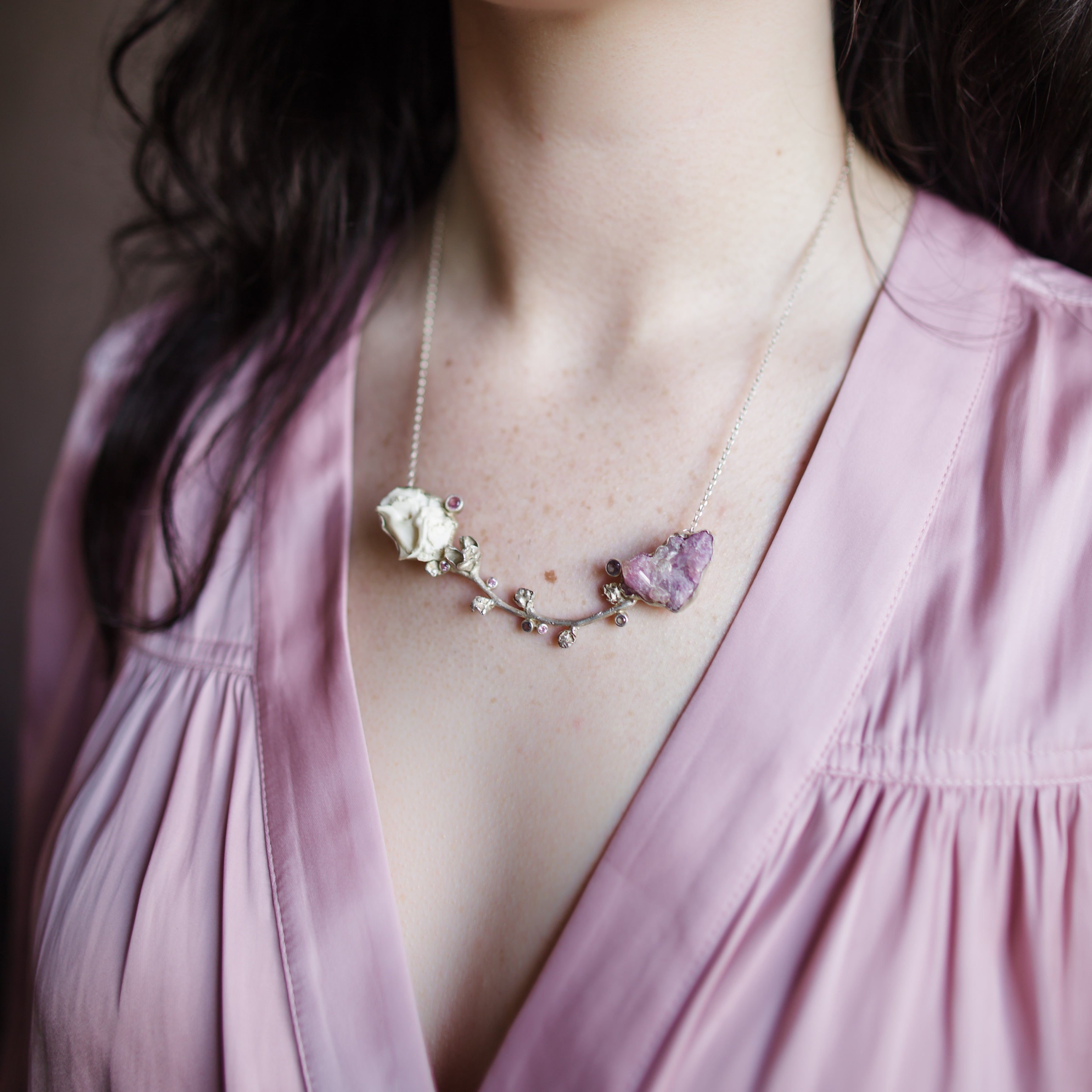 A woman wearing a silver cast brooch with a combination of Vesuvianite and tourmaline stones that can double as a necklace handmade in USA by North Carolina Jewelry artist Anna Johnson