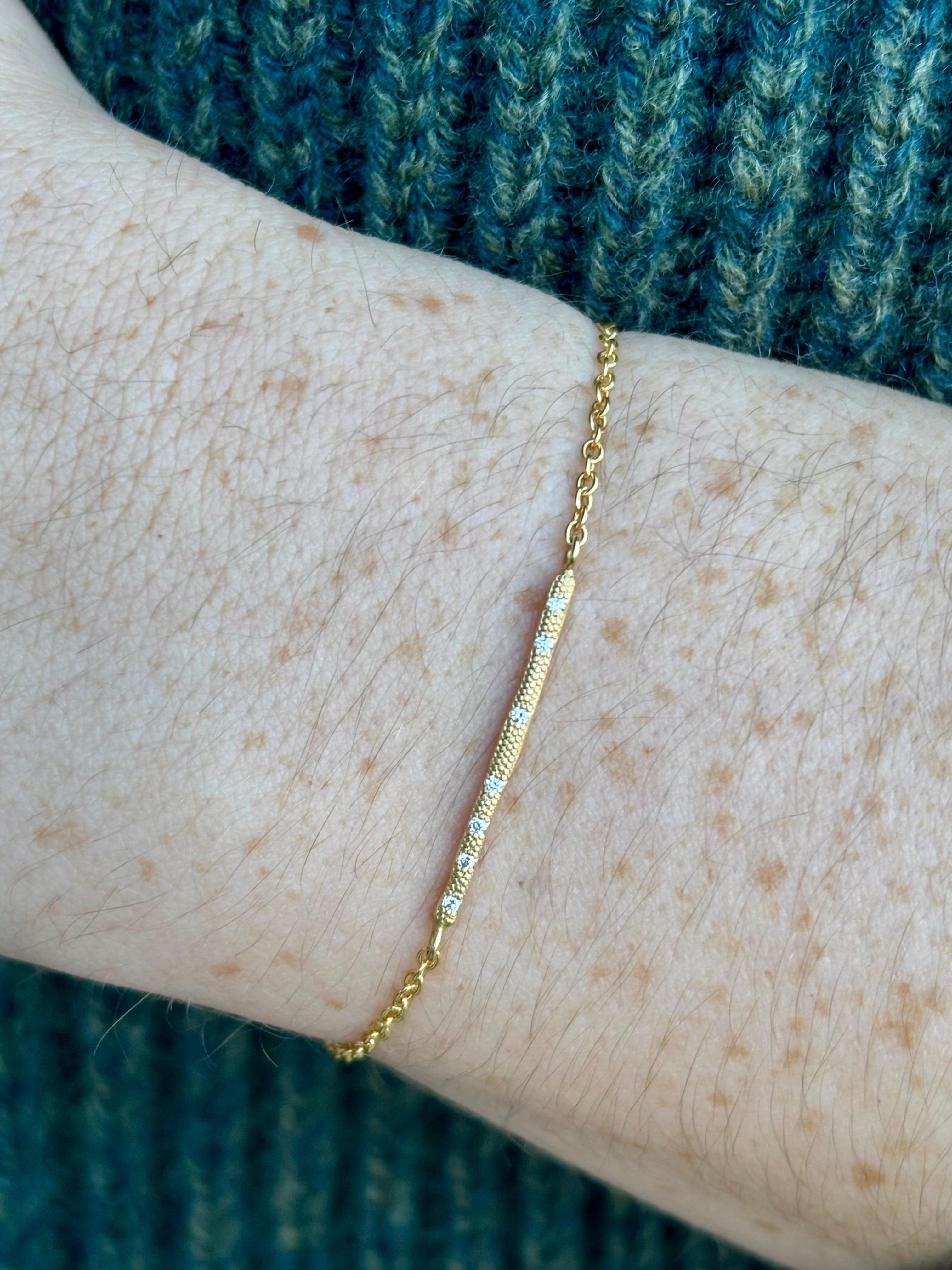 Image of a woman wearing designer Anne Sportun 18 carat gold diamond stardust bracelet single bar with hammered texture and adjustable clasp