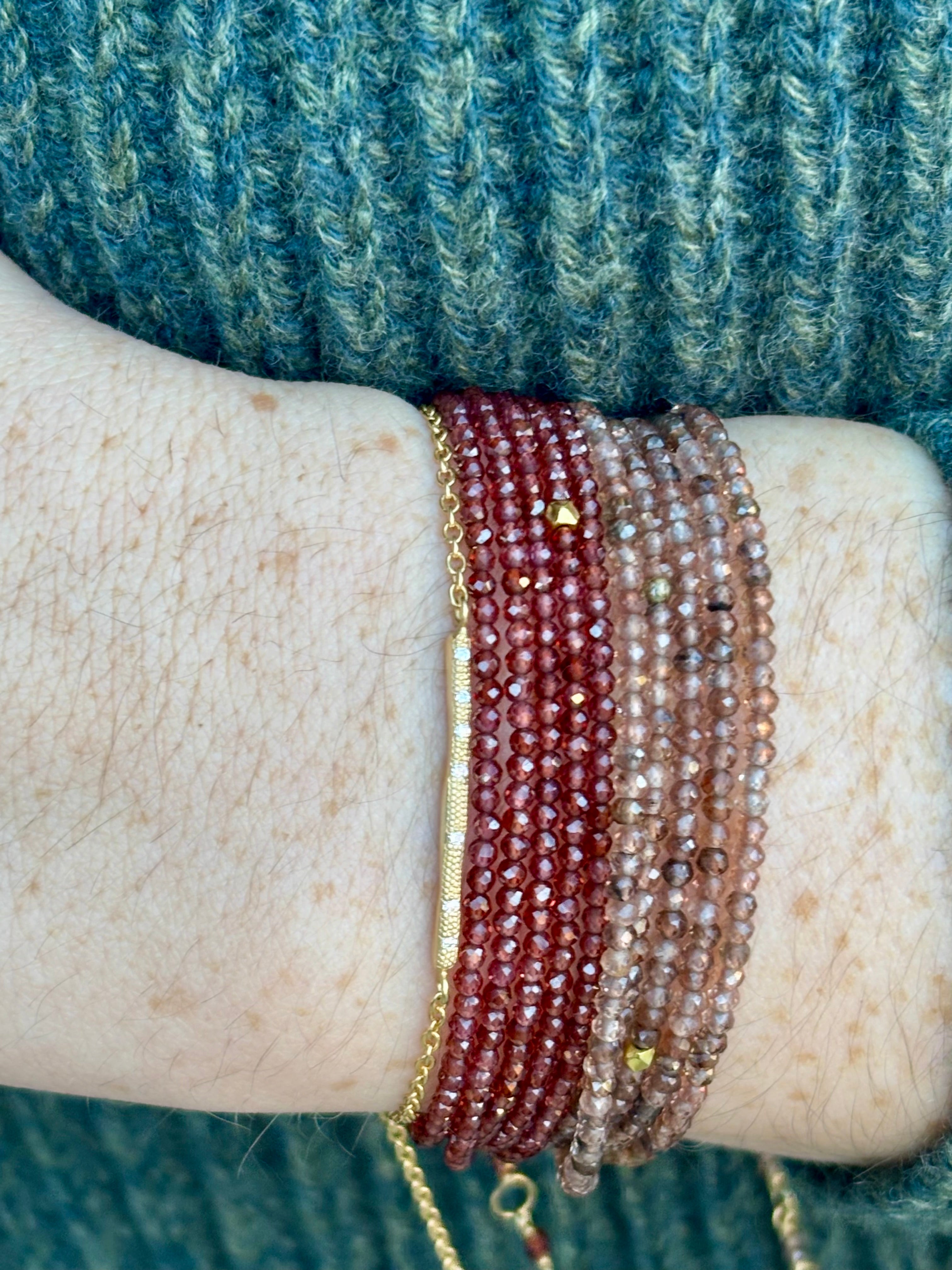 Image of woman wearing a stack of Canadian jewelry designer Anne Sportun bracelets with diamonds, 18k yellow gold and garnets