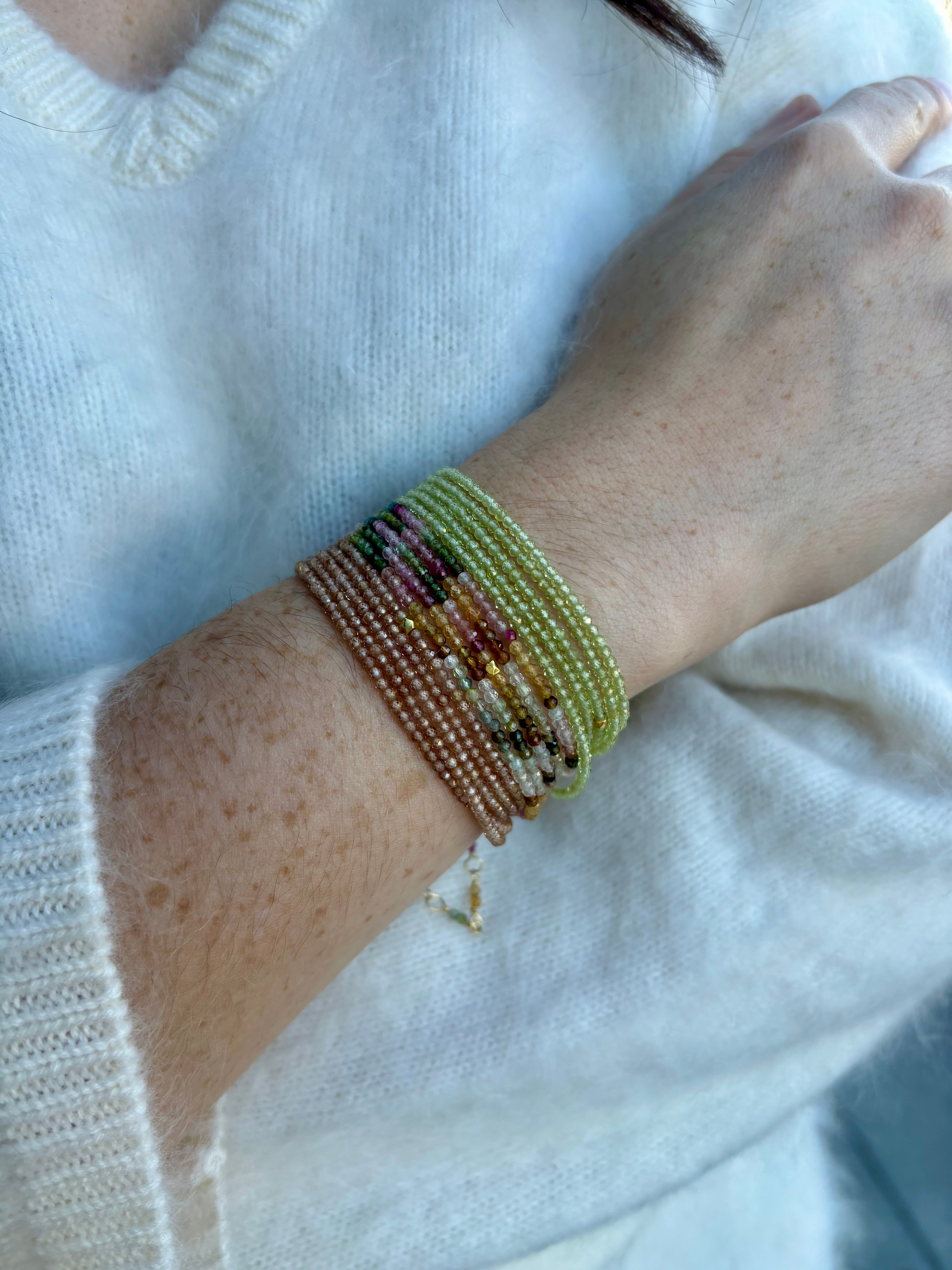 Image of a woman wearing premium jewelry stacked peridot, tourmaline, and garnet bracelets by Canadian designer Anne Sportun