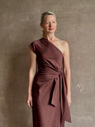 Mature woman wearing Apiece Apart brown comfy jersey cotton maxi dress one shoulder twist tie waist stretch