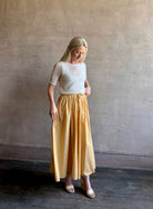 Mature woman wearing the Hanne Tie Maxi Skirt from Apiece Apart rendered in a butter yellow hue and crafted from 100% organic cotton with adjustable drawstring and elastic waistband
