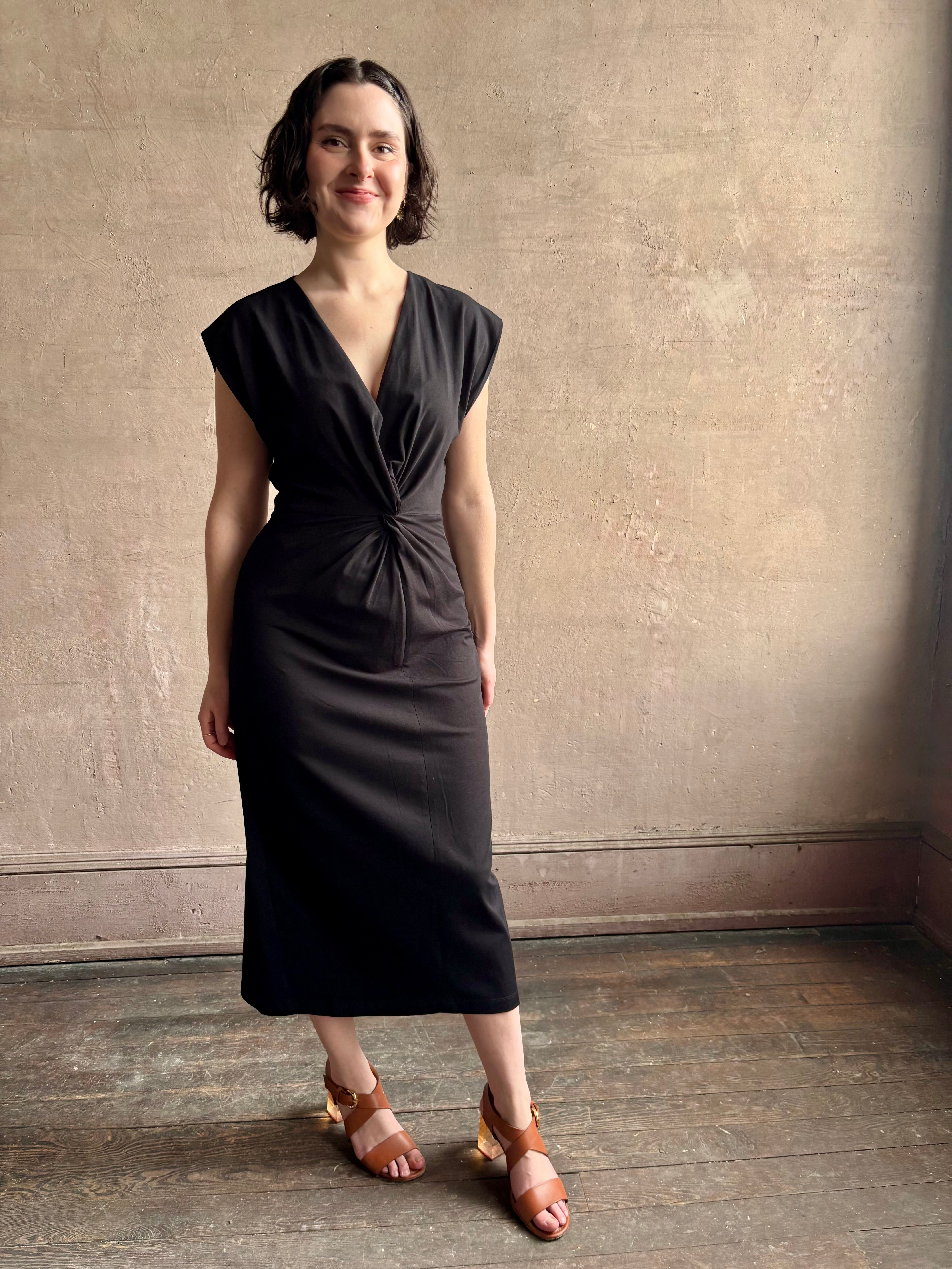 Woman wearing a timeless Twist Front Column Dress from Apiece Apart in a comfortable black cotton jersey midi that can transition day to night