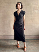 Woman wearing a timeless Twist Front Column Dress from Apiece Apart in a comfortable black cotton jersey midi that can transition day to night