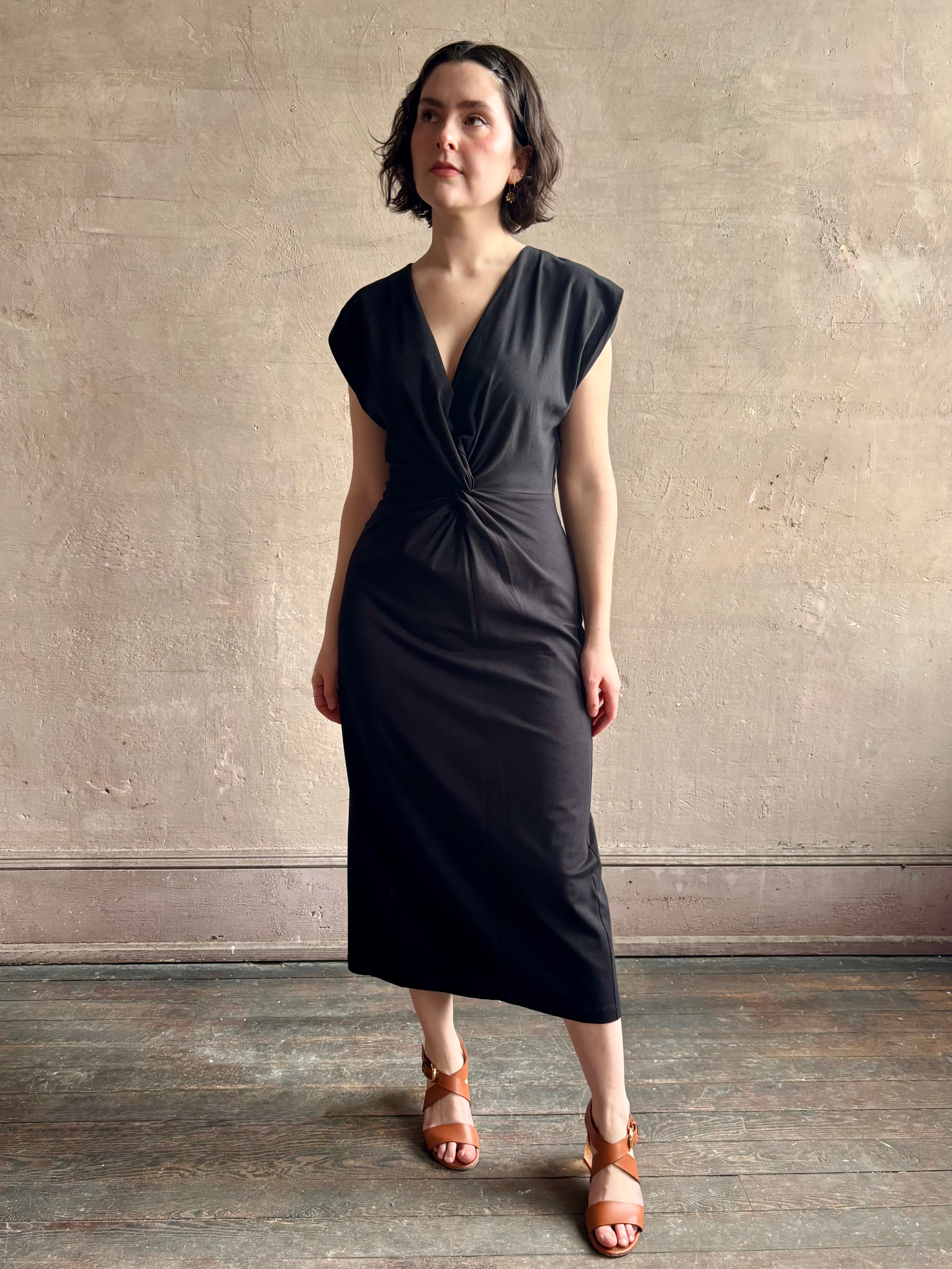 Woman wearing a timeless Twist Front Column Dress from Apiece Apart in a comfortable black cotton jersey midi that can transition day to night