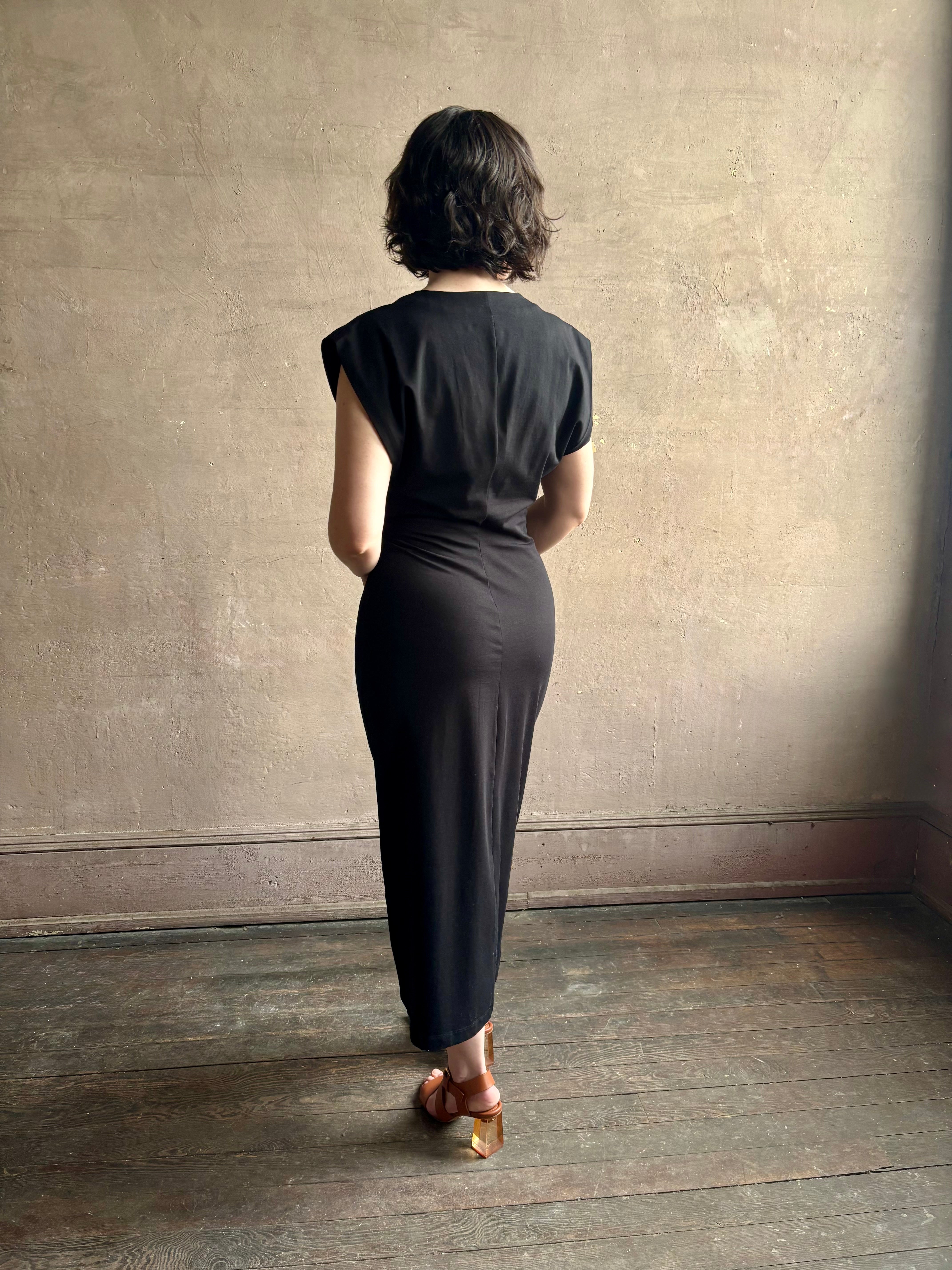 Woman wearing a timeless Twist Front Column Dress from Apiece Apart in a comfortable black cotton jersey midi that can transition day to night