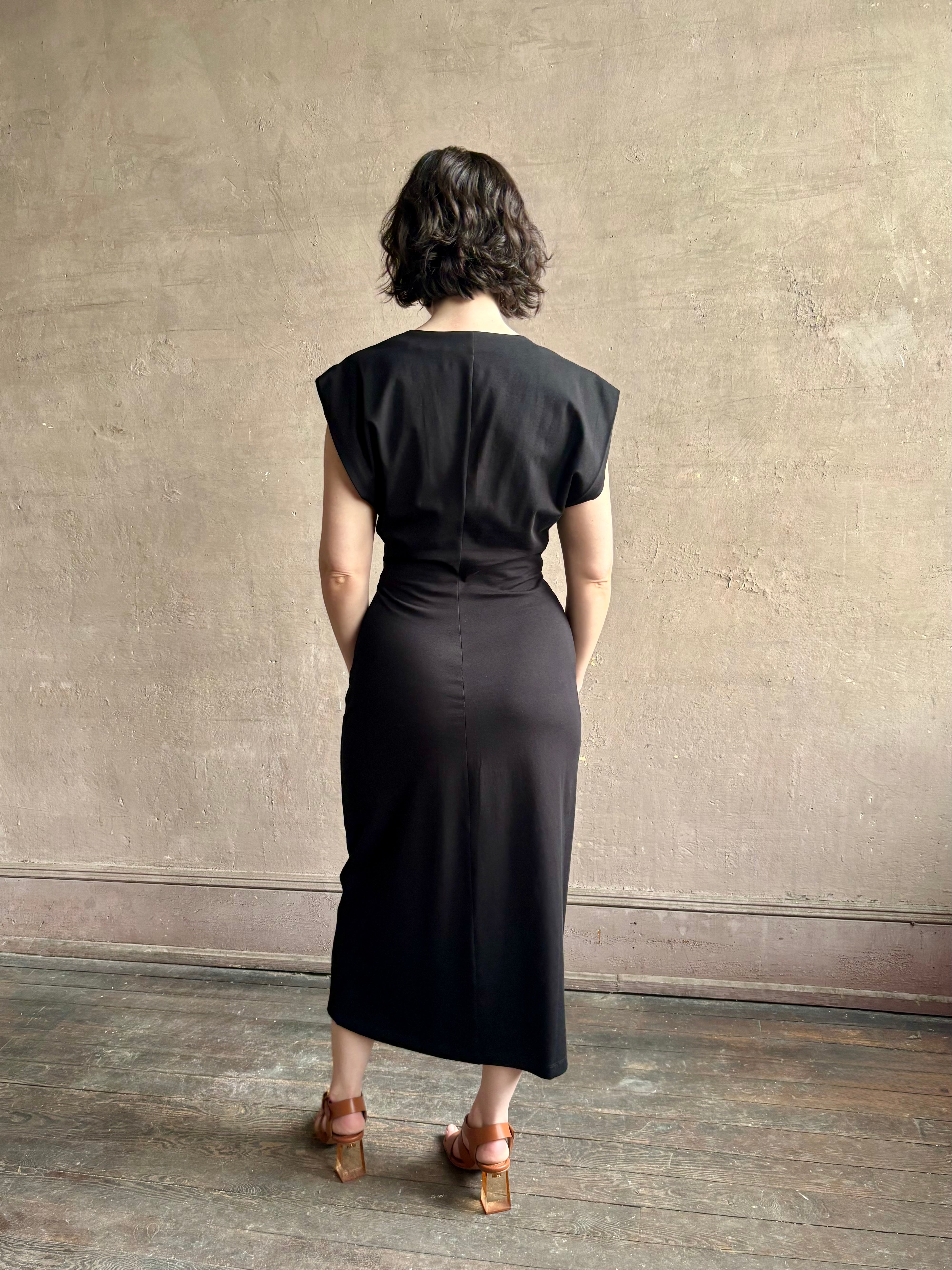 Woman wearing a timeless Twist Front Column Dress from Apiece Apart in a comfortable black cotton jersey midi that can transition day to night
