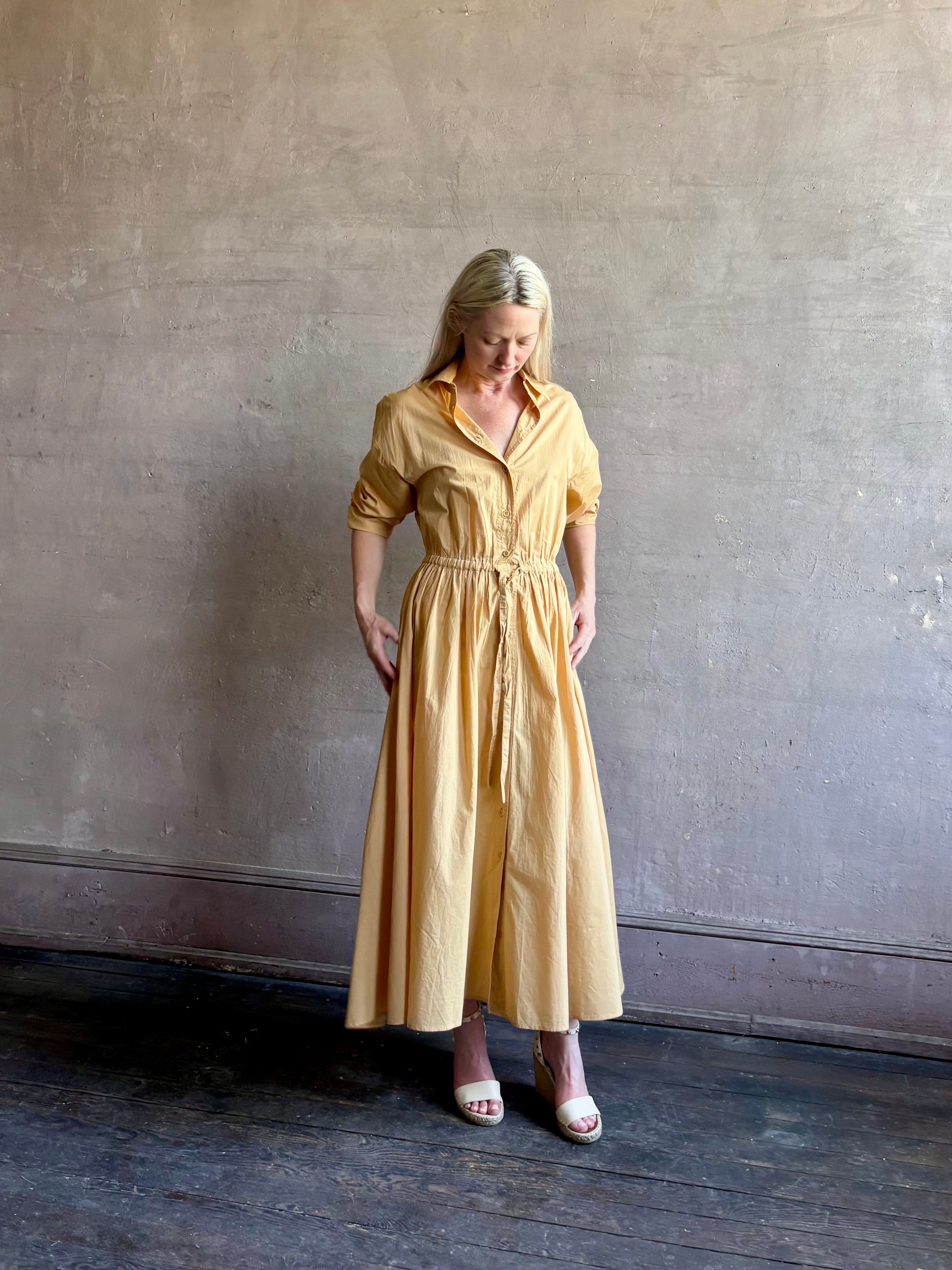 Image of mature woman wearing the Priska Shirt Dress from Apiece Apart rendered in a butter yellow and crafted from 100% organic cotton featuring long sleeves, collared button front and adjustable drawstring waistband