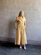Image of mature woman wearing the Priska Shirt Dress from Apiece Apart rendered in a butter yellow and crafted from 100% organic cotton featuring long sleeves, collared button front and adjustable drawstring waistband