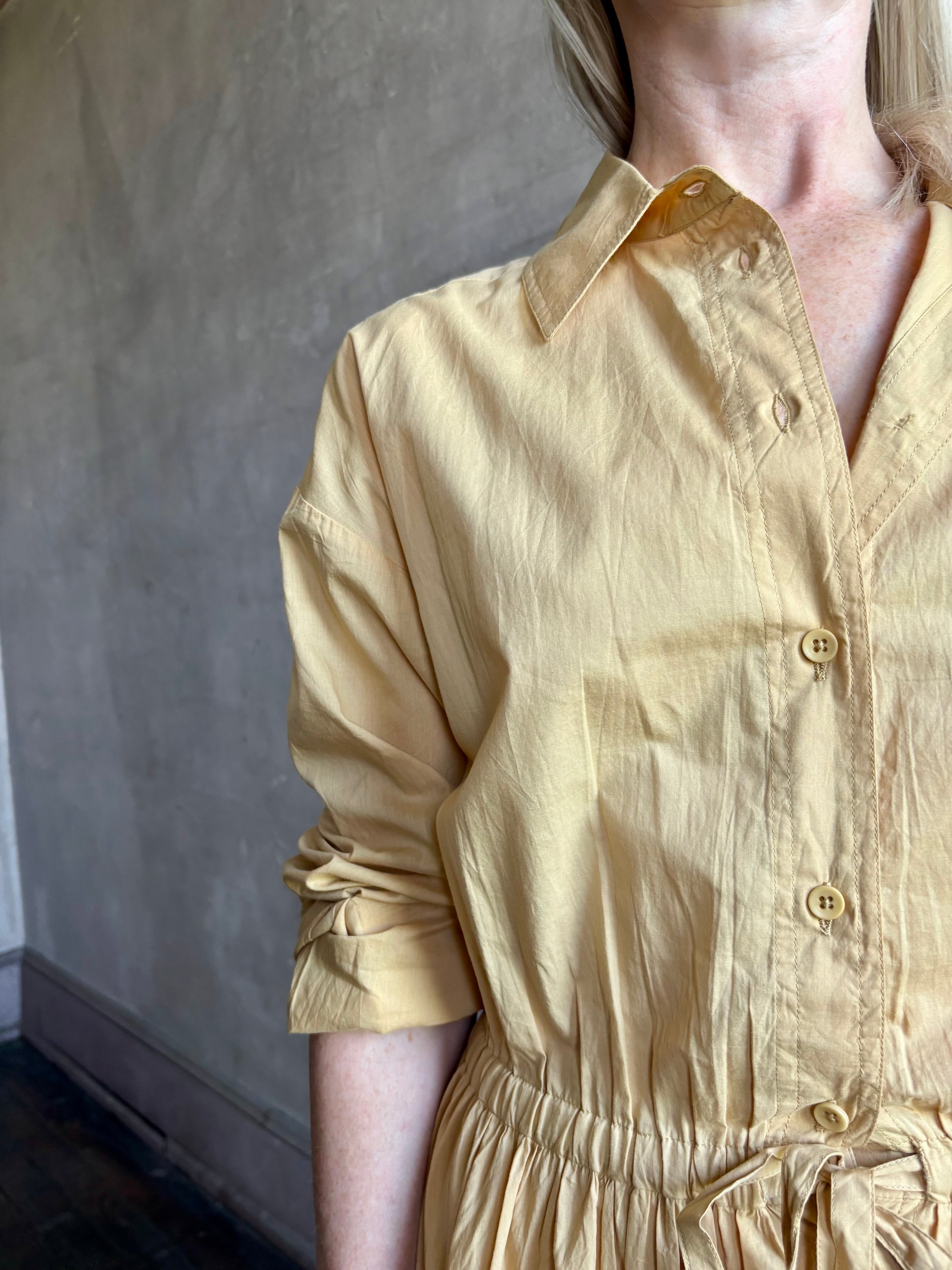 Image of mature woman wearing the Priska Shirt Dress from Apiece Apart rendered in a butter yellow and crafted from 100% organic cotton featuring long sleeves, collared button front and adjustable drawstring waistband