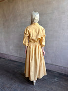 Image of mature woman wearing the Priska Shirt Dress from Apiece Apart rendered in a butter yellow and crafted from 100% organic cotton featuring long sleeves, collared button front and adjustable drawstring waistband