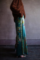 Image featuring a woman wearing the silk Franca pants by Alemais with a drawstring waist and wide leg paisley print in turquoise.