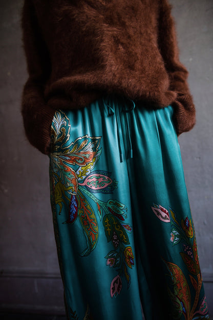 Image featuring a woman wearing the silk Franca pants by Alemais with a drawstring waist and wide leg paisley print in turquoise.