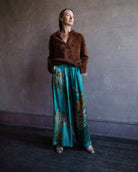 Image featuring a woman wearing the silk Franca pants by Alemais with a drawstring waist and wide leg paisley print in turquoise.