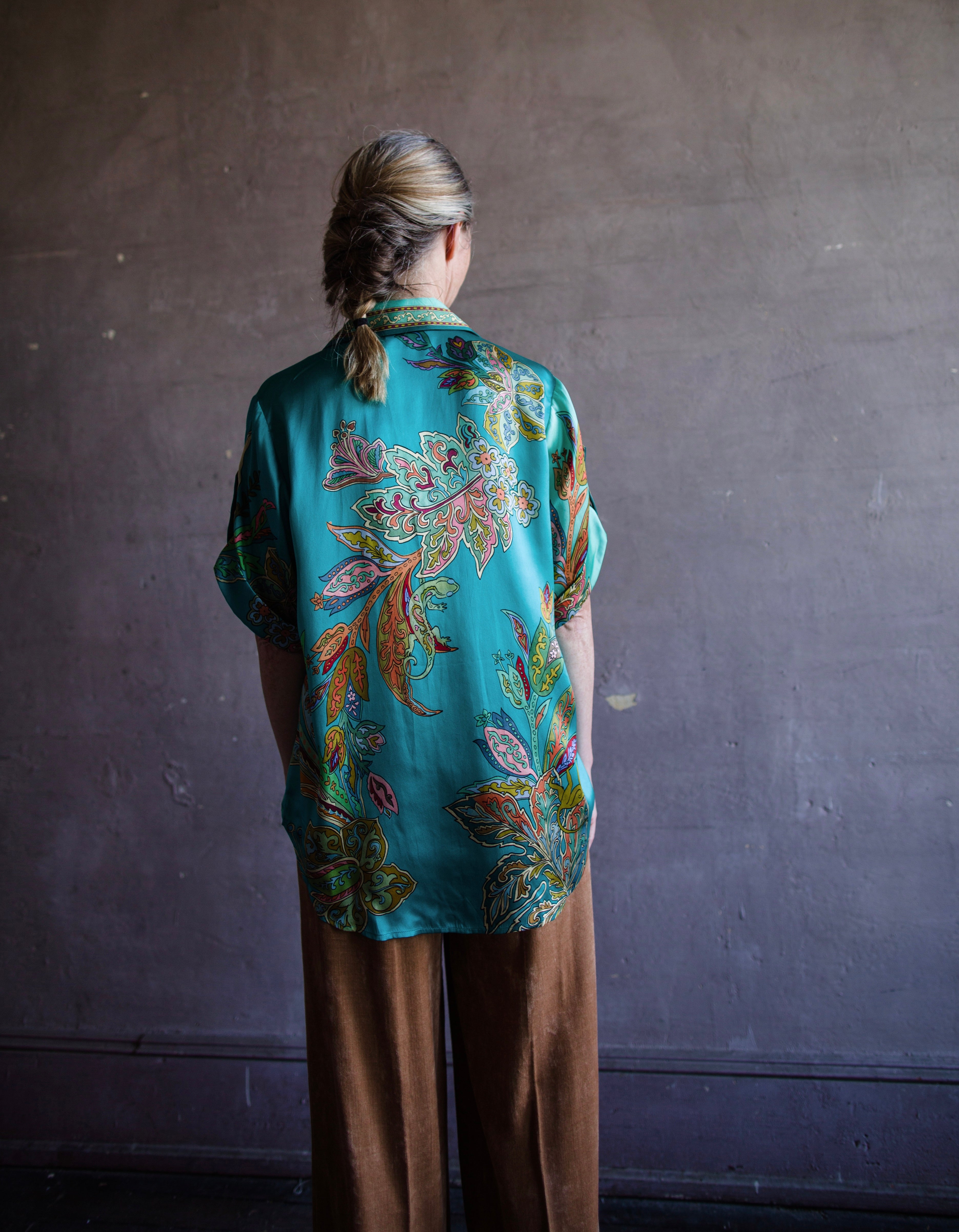 Image featuring a woman wearing the silk Franca button up top by Alemais with a rolled sleeve and relaxed fit in turquoise.