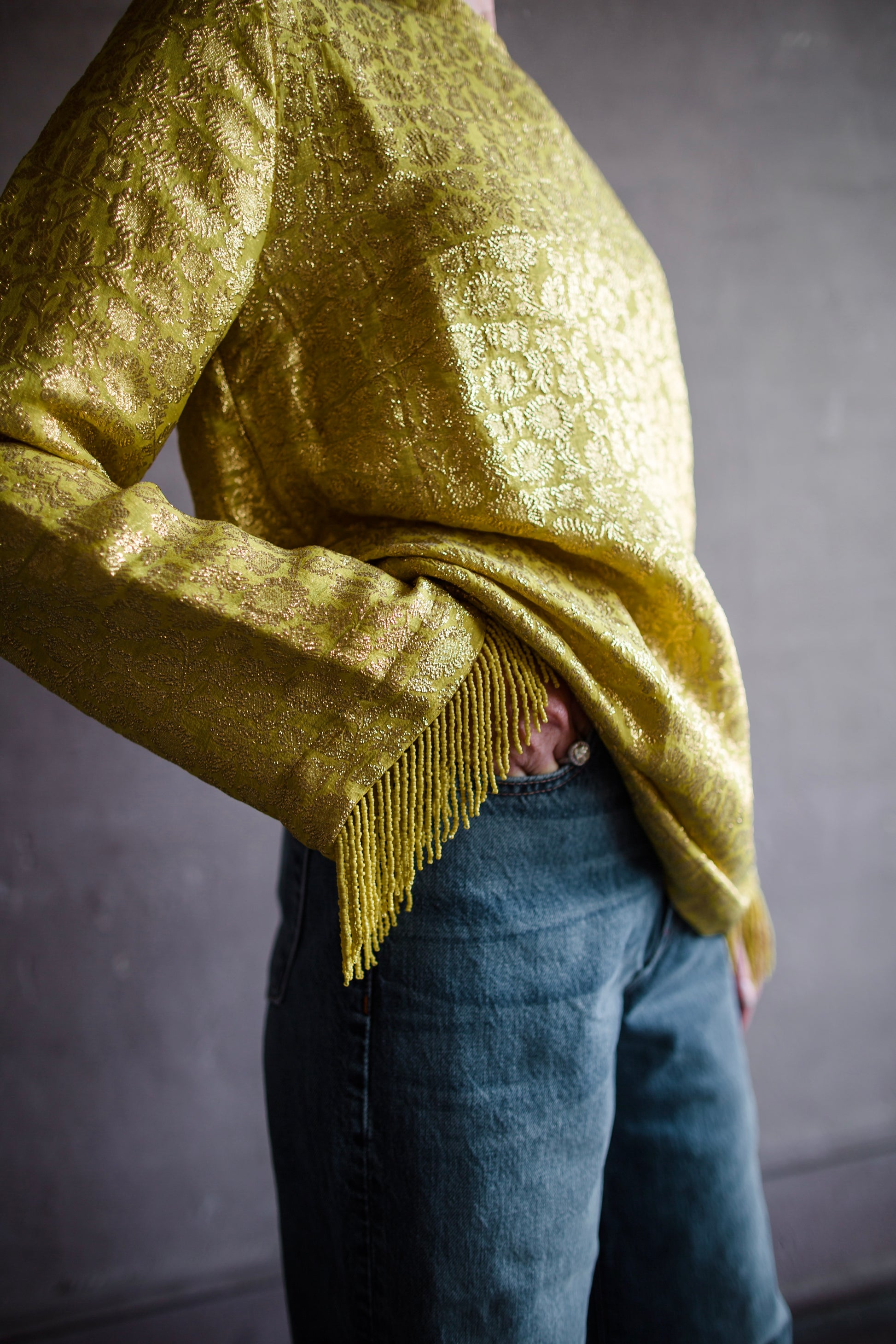 Image featuring a woman wearing the yellow Astra top by Alemais features a crew neckline with brocade texture and beaded fringe trim.