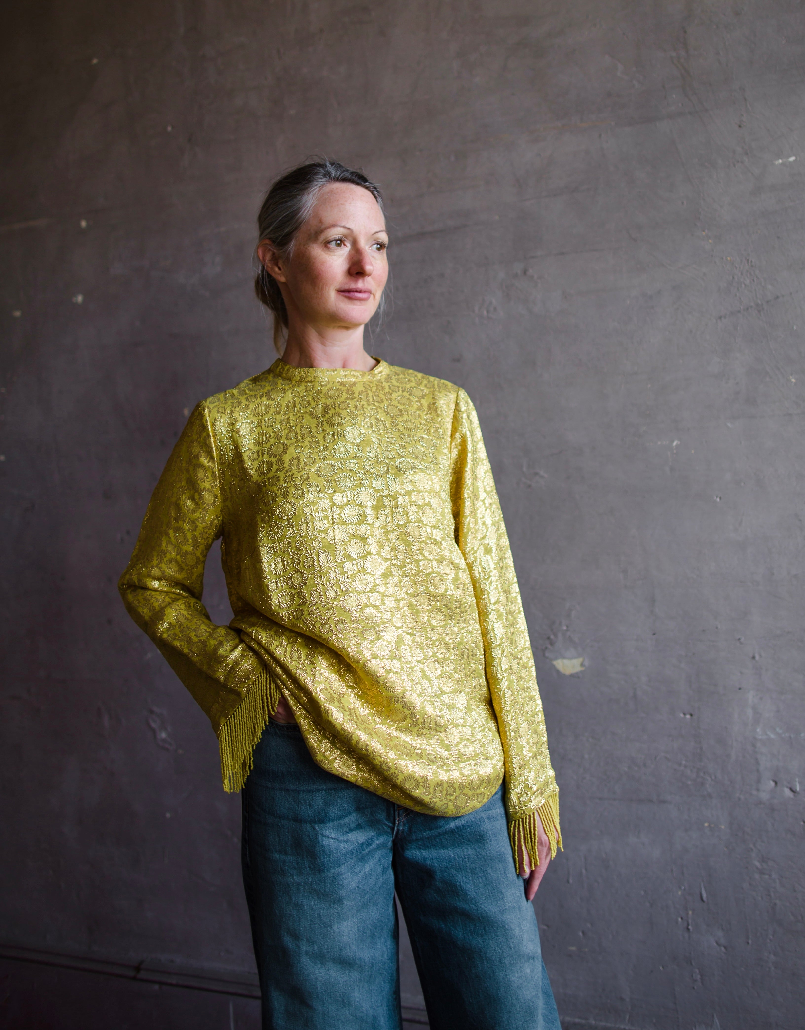 Image featuring a woman wearing the yellow Astra top by Alemais features a crew neckline with brocade texture and beaded fringe trim.